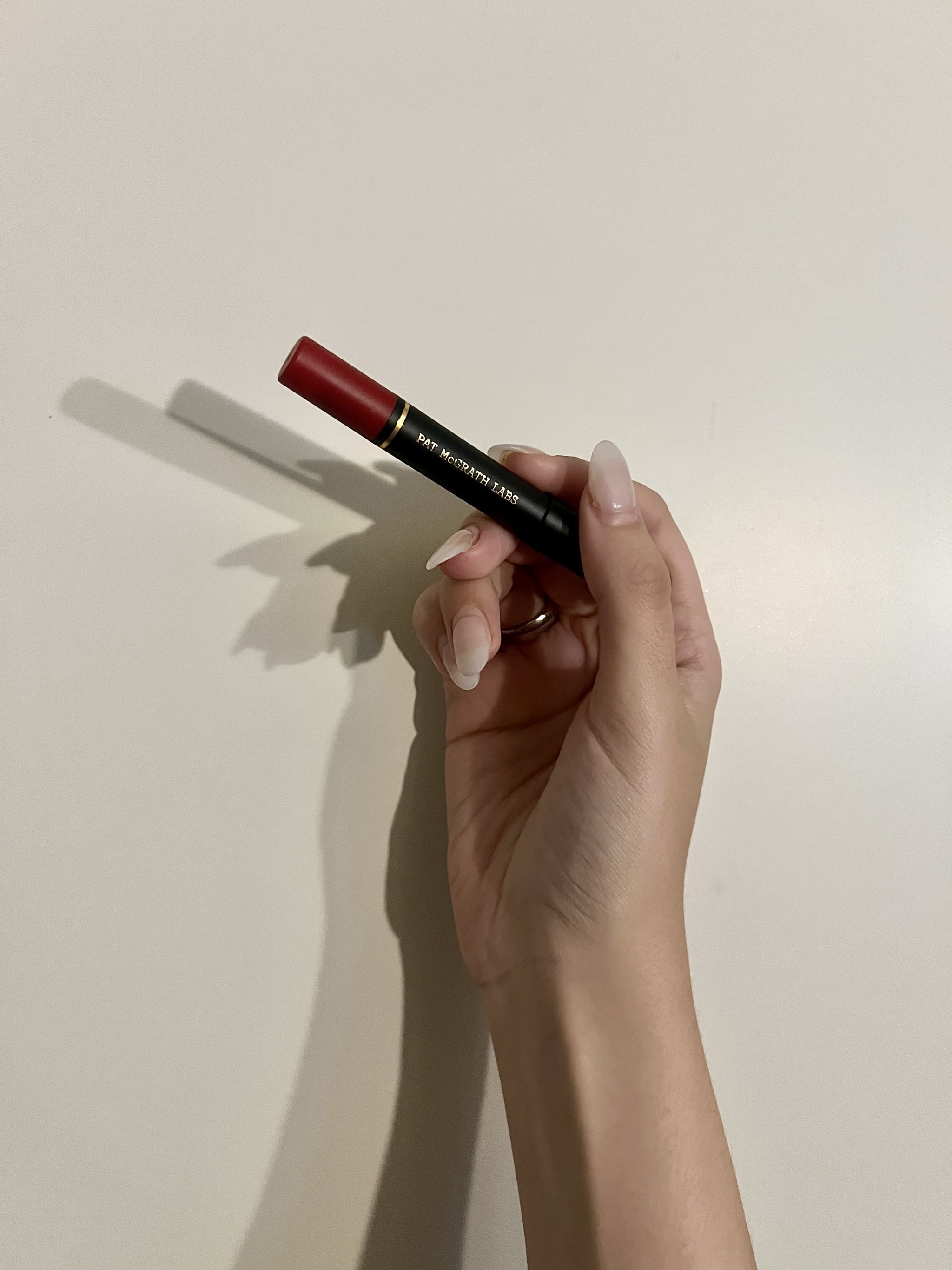 a woman's hand holding the Pat McGrath Labs Dramatique Mega Lip Pencil in Elson red against a white wall