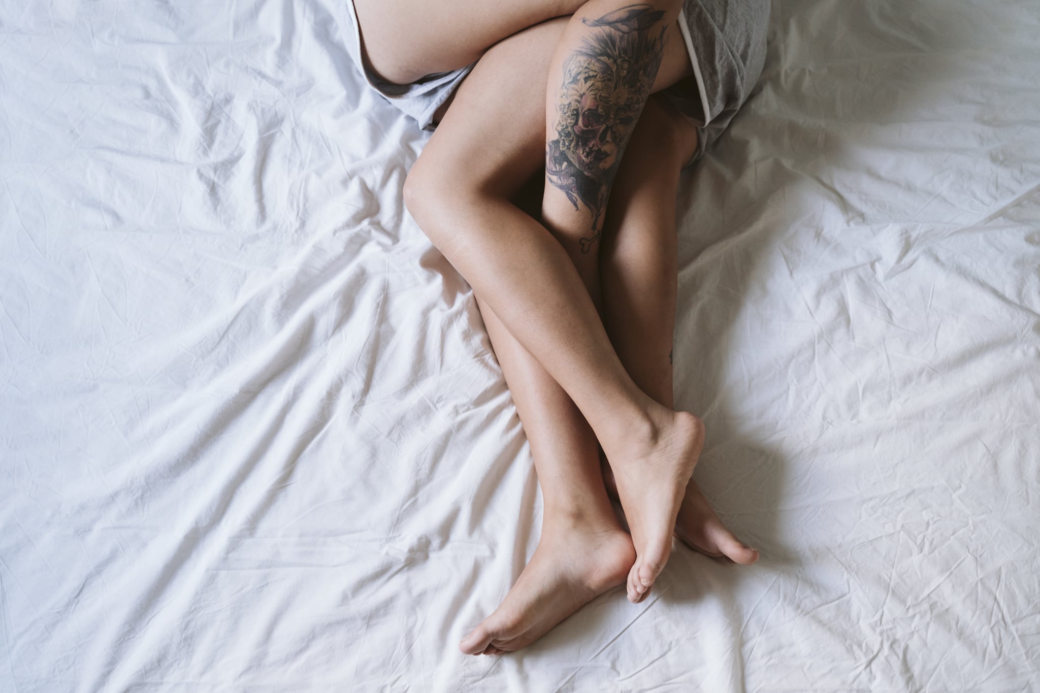 Two pairs of legs are intertwined under the covers on a white bed