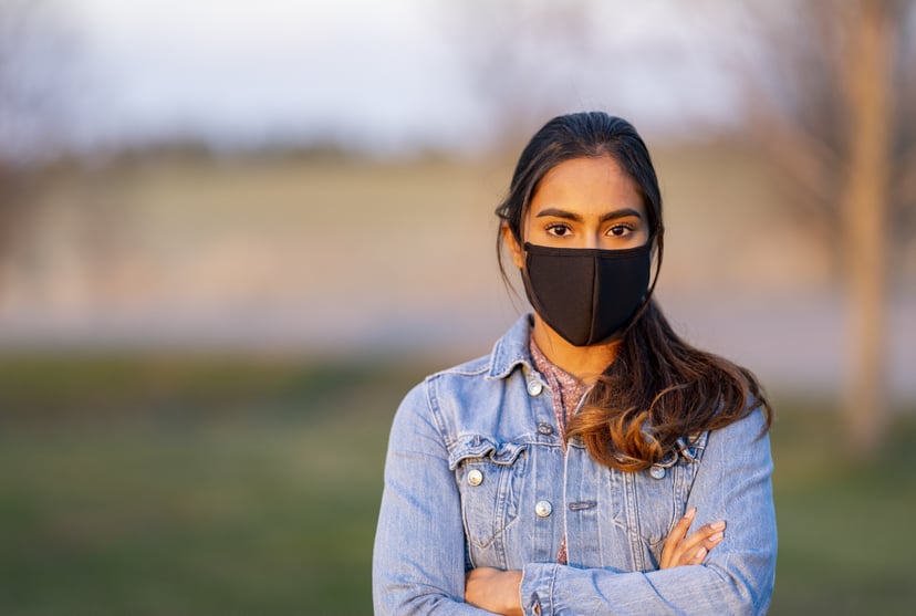 Ethnic girl standing outside wearing a protective mask during a beautiful sunset.