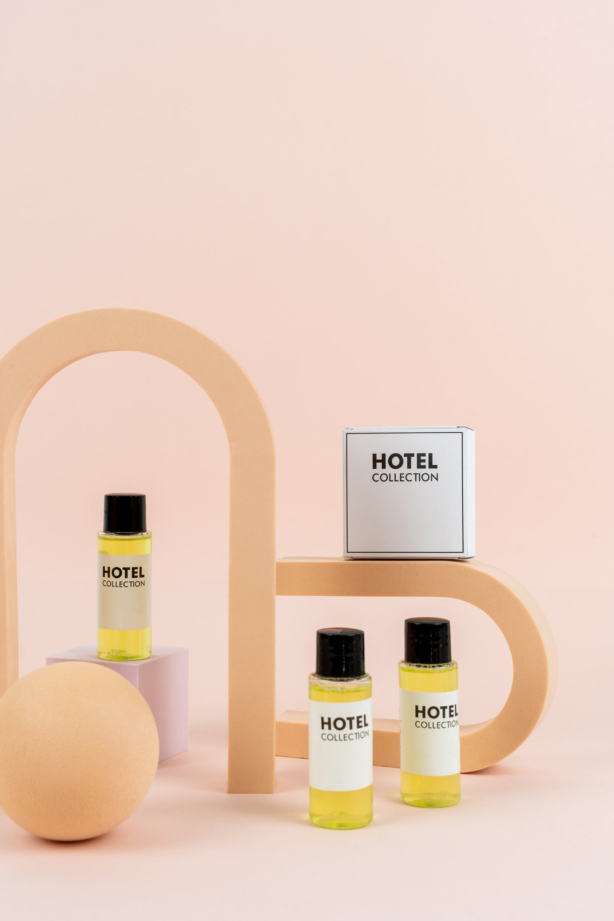 Set of hotel toiletries collection with travel pack of shower gel, soap, shampoo and hair conditioner close to geometric shapes against pastel pink background with copy space.  Advertising concept