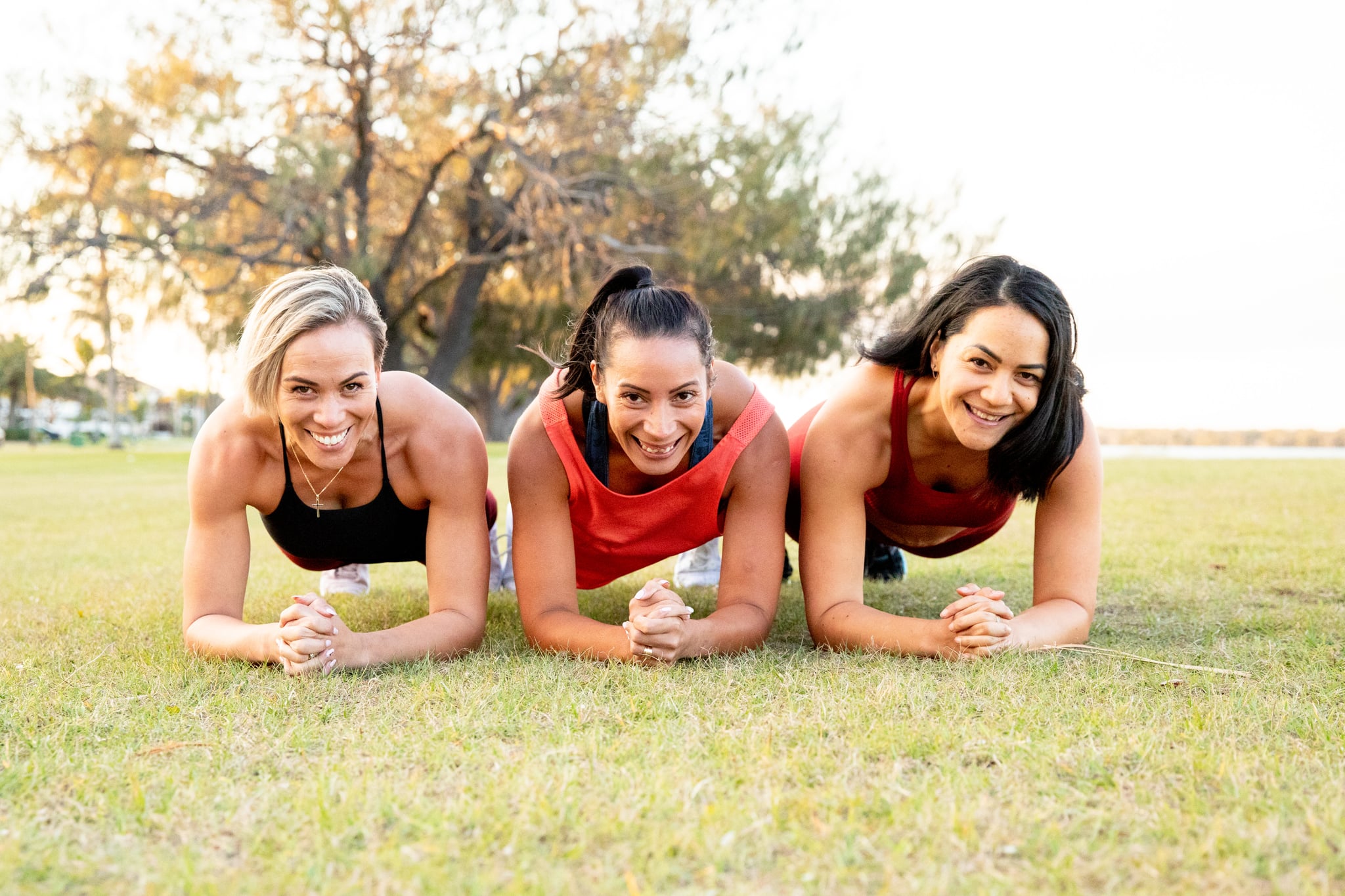 Three strong women working out together to keep fit, healthy and happy by the beach in active wear. Lifting weights, running and building core strength.