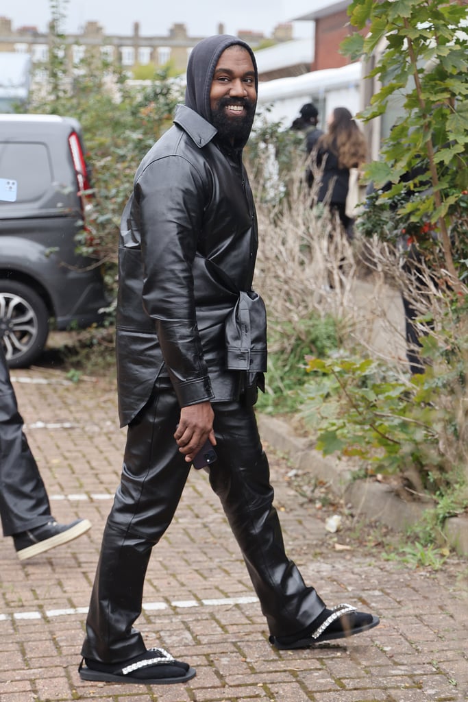 On Sept. 26, Kanye West attended Burberry's spring/summer 2023 show at London Fashion Week, and as usual, his surprise appearance sparked discussions across social media. While the rapper and fashion designer opted for his signature hoodie-and-leather-jacket combo, he went rogue with his footwear: black socks paired with studded glitter flip-flops. 
Presumably wearing pieces from Burberry, West's black ensemble consisted of leather pants and a matching button-down jacket with sleeves tied around the waist, which he layered over a dark hoodie. In contrast, his slippers looked to be made of foam — yes, like the ones they offer at the nail salon — and lined with silver crystals along the straps. 
Inspired by the British seaside, Burberry's rescheduled runway show welcomed Naomi Campbell, Bella Hadid, Irina Shayk, and more strutting down the catwalk in layered, deconstructed looks mixing both underwear and outerwear. West sat in the star-studded front row alongside celebrities like Stormzy, Erykah Badu, Normani, Lori Harvey, and Chlöe and posed for a photo with Campbell backstage after the show. 
It's certainly not the first time West's outfits and style choices have sparked confusion among fans and critics alike. Many were not fans of the Yeezy founder's chunky moon boots, which he wore practically everywhere in recent months, and his full-body mask at the BET Awards in June left many concerned. His latest appearance comes a week following the official termination of West and Gap's Yeezy partnership, which produced a collection that was reportedly sold out of trash bags in stores. 
Ahead, see more photos of West's polarizing outfit at London Fashion Week.

    Related:

            
            
                                    
                            

            Vanessa Hudgens Styled a Chain-Mail Bandeau Top With 6-Inch Heels For Versace