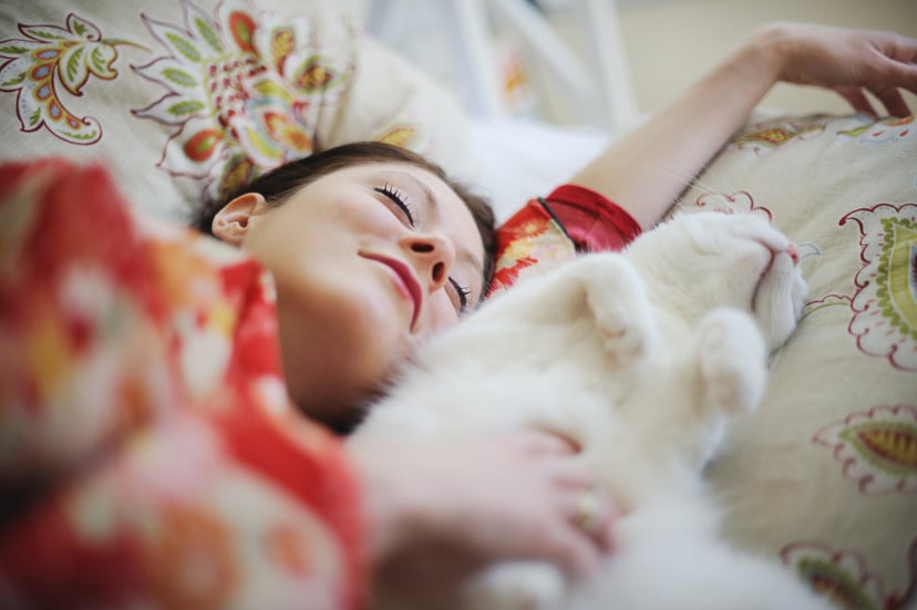 Smiling woman wearing  kimono, in bed, asleep next to white cat.