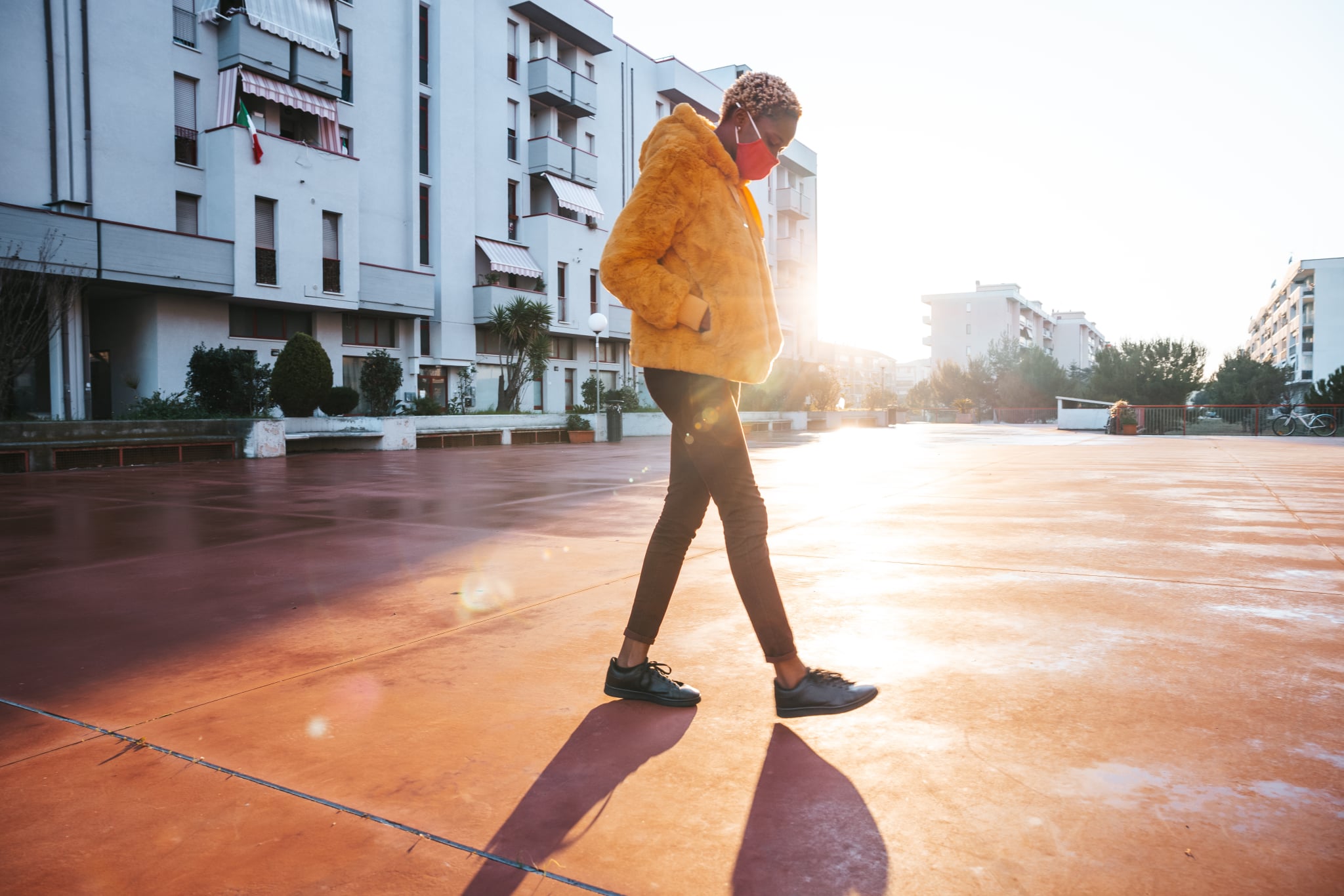 Young woman walking in the neighborhood wearing a yellow coat with a pink cloth mask.