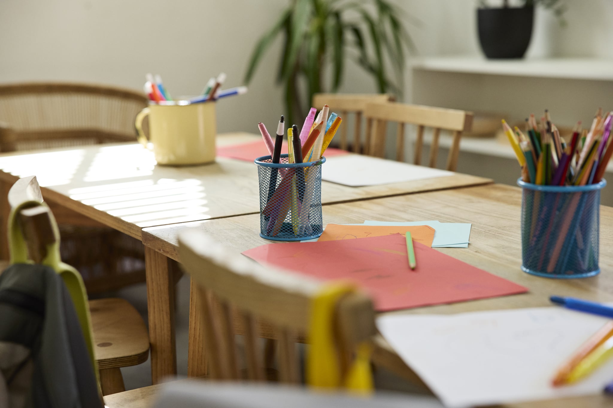 Colored pencils kept in containers on table near papers in empty classroom at school