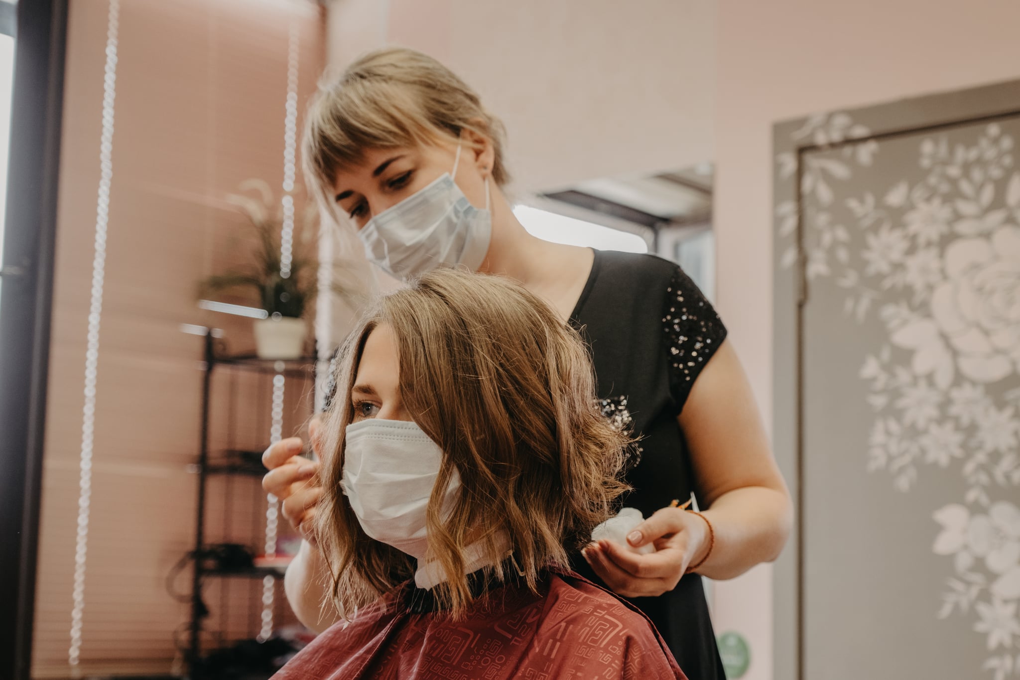 Young woman have hair cutting at hair stylist during pandemic isolation, they both wear protective equipment