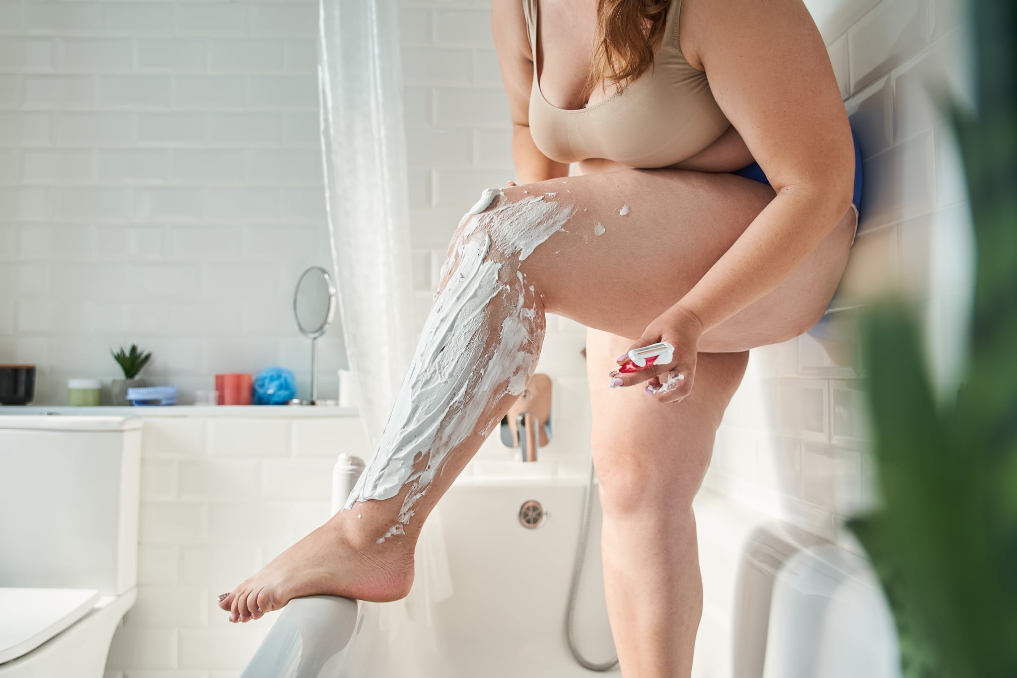 一个大码的女人在浴室里刮腿毛，这是她日常个人护理的一部分