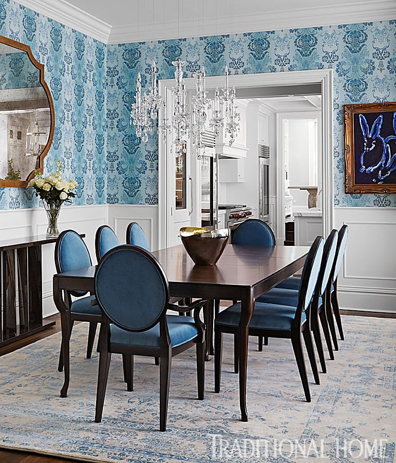 Blue is once again prominent in the dining room thanks to the printed wallpaper and chairs. A piece of bunny art by Hunt Slonem hangs on the wall. The chandelier is from Windfall.