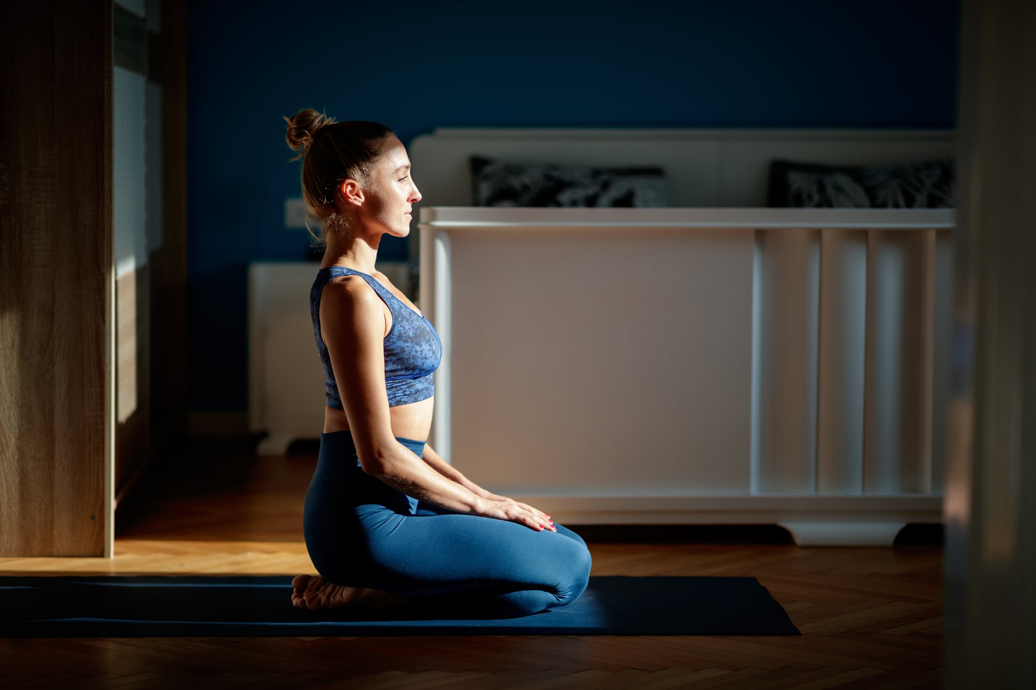 Mid adult woman meditating at home, sitting on toga mat