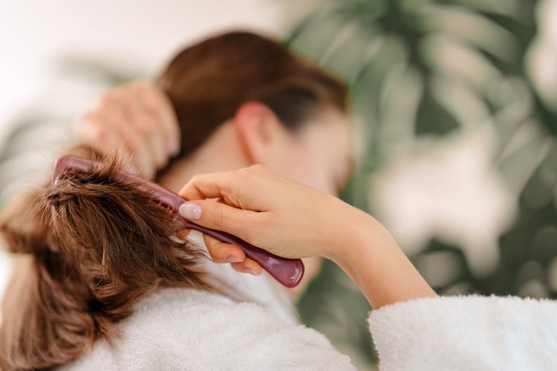 Rear view of young woman combing her hair. Morning routine concept.