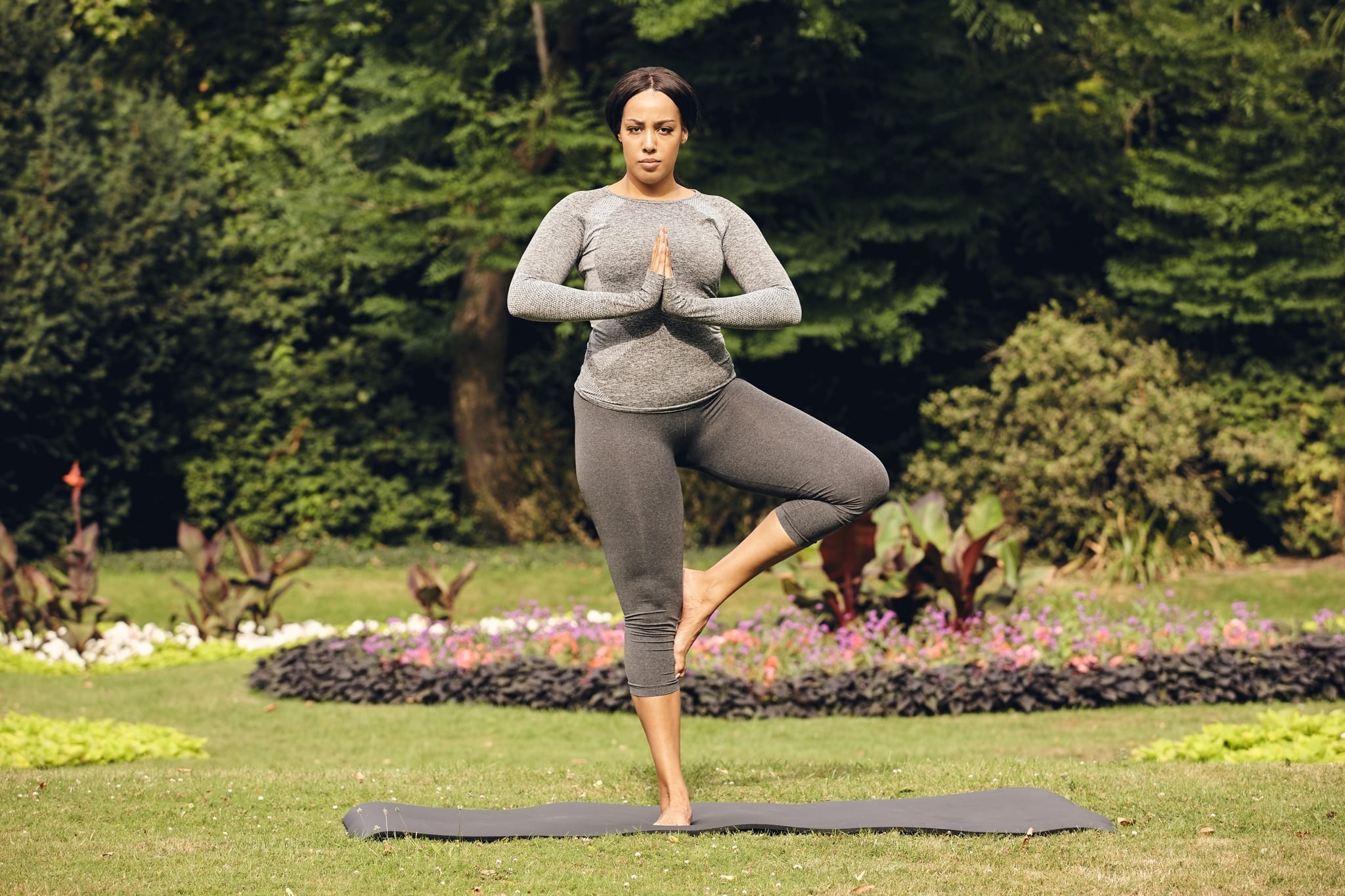 Full length portrait of healthy woman practicing yoga in the park. Fitness woman doing tree pose yoga.