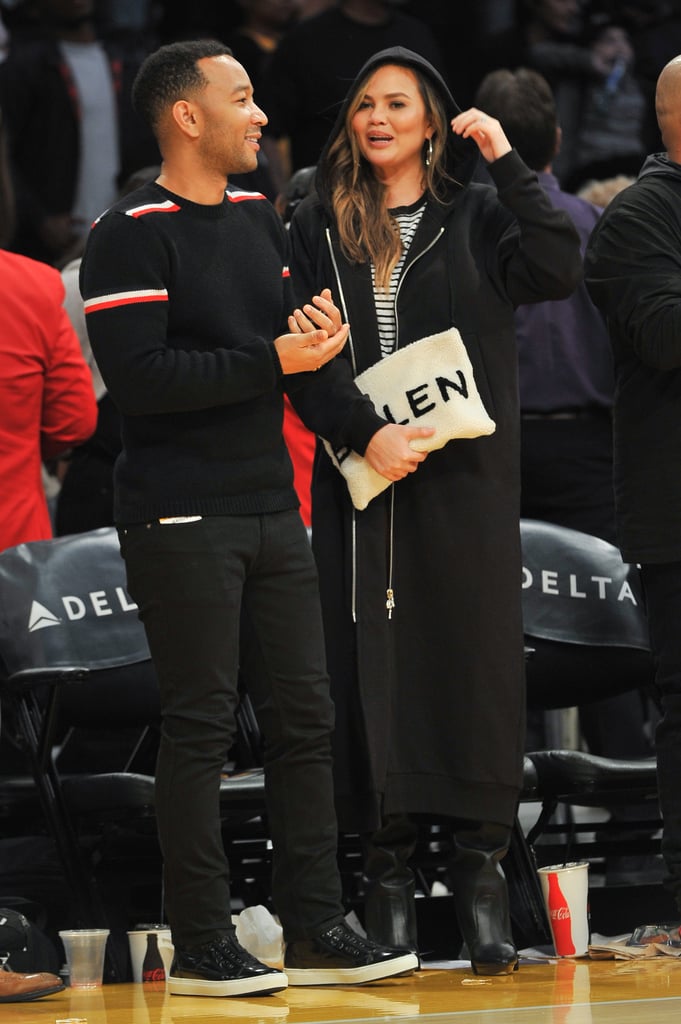Chrissy attended a basketball game wearing a long black hoodie, striped shirt, and leather boots. She carried a white Balenciaga clutch and accessorized with Svelte Metals hoops.