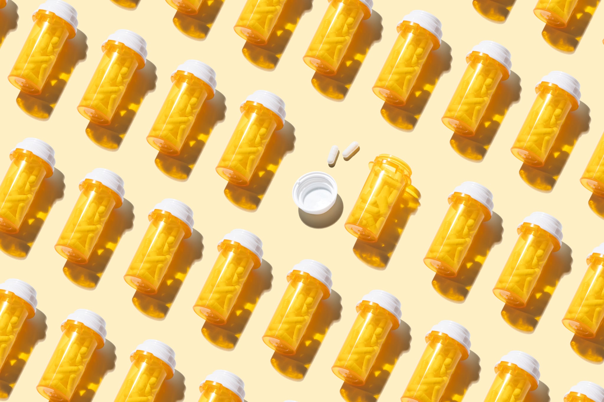 打开处方药瓶子在许多其他密封的瓶子在黄色背景高角度视图。