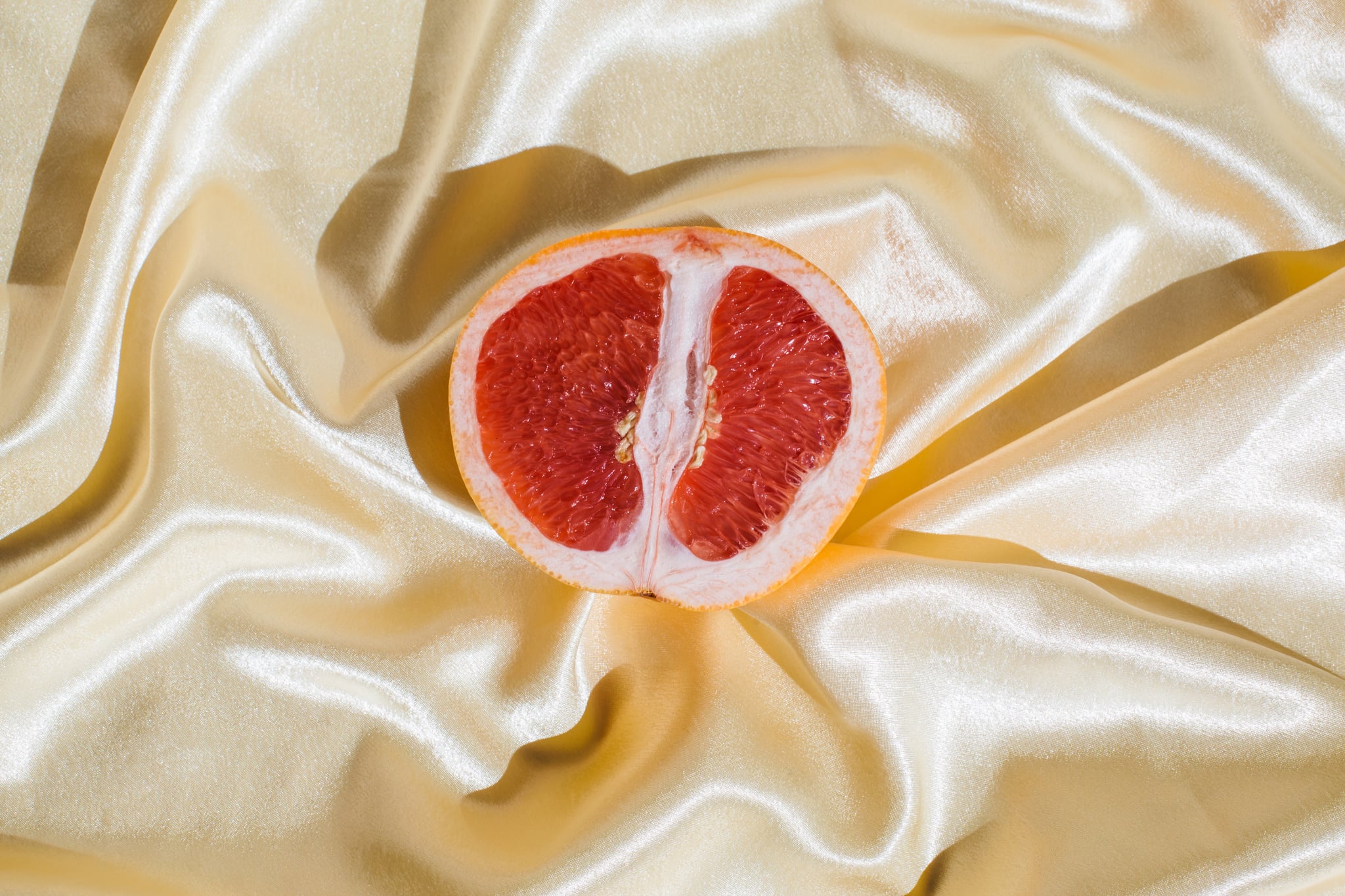 Fresh grapefruit on beige soft silk fabric background. Sex concept. Women's health, sexuality, erotic tension. Female vagina and clitoris symbol.