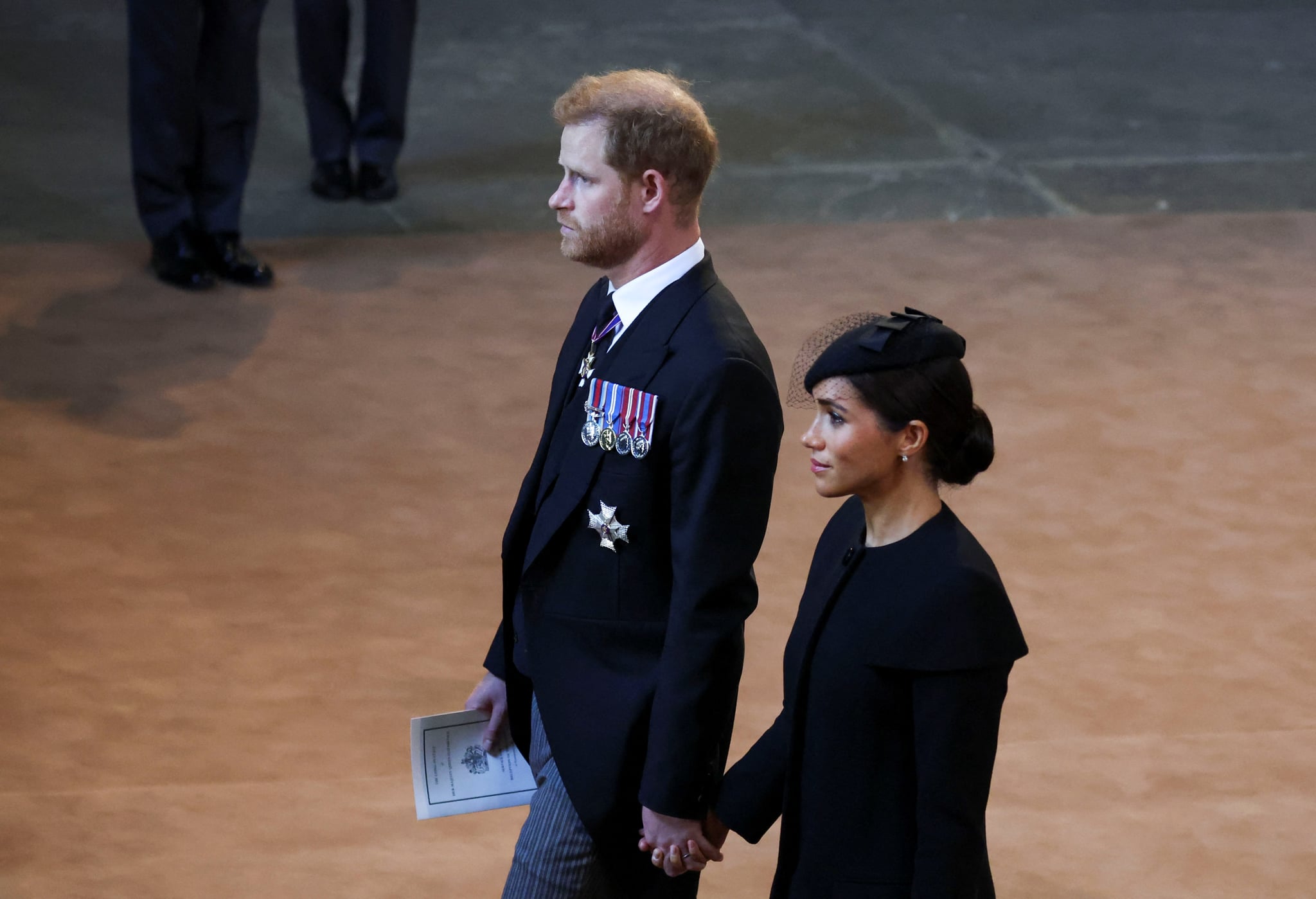 LONDON, ENGLAND - SEPTEMBER 14: Prince Harry and Meghan, Duchess of Sussex walk as procession with the coffin of Britain's Queen Elizabeth arrives at Westminster Hall from Buckingham Palace for her lying in state on September 14, 2022 in London, United Kingdom. Queen Elizabeth II's coffin is taken in procession on a Gun Carriage of The King's Troop Royal Horse Artillery from Buckingham Palace to Westminster Hall where she will lay in state until the early morning of her funeral. Queen Elizabeth II died at Balmoral Castle in Scotland on September 8, 2022, and is succeeded by her eldest son, King Charles III. (Photo by Phil Noble - WPA Pool/Getty Images)