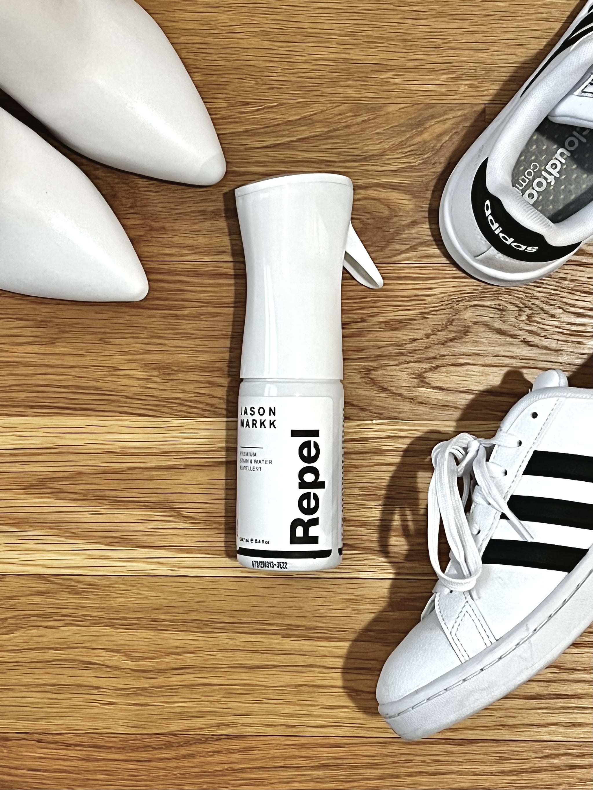 Jason Markk Repel Spray in the middle with a pair of white pointy-toe boots in the left hand corner and Adidas white sneakers on the right side.