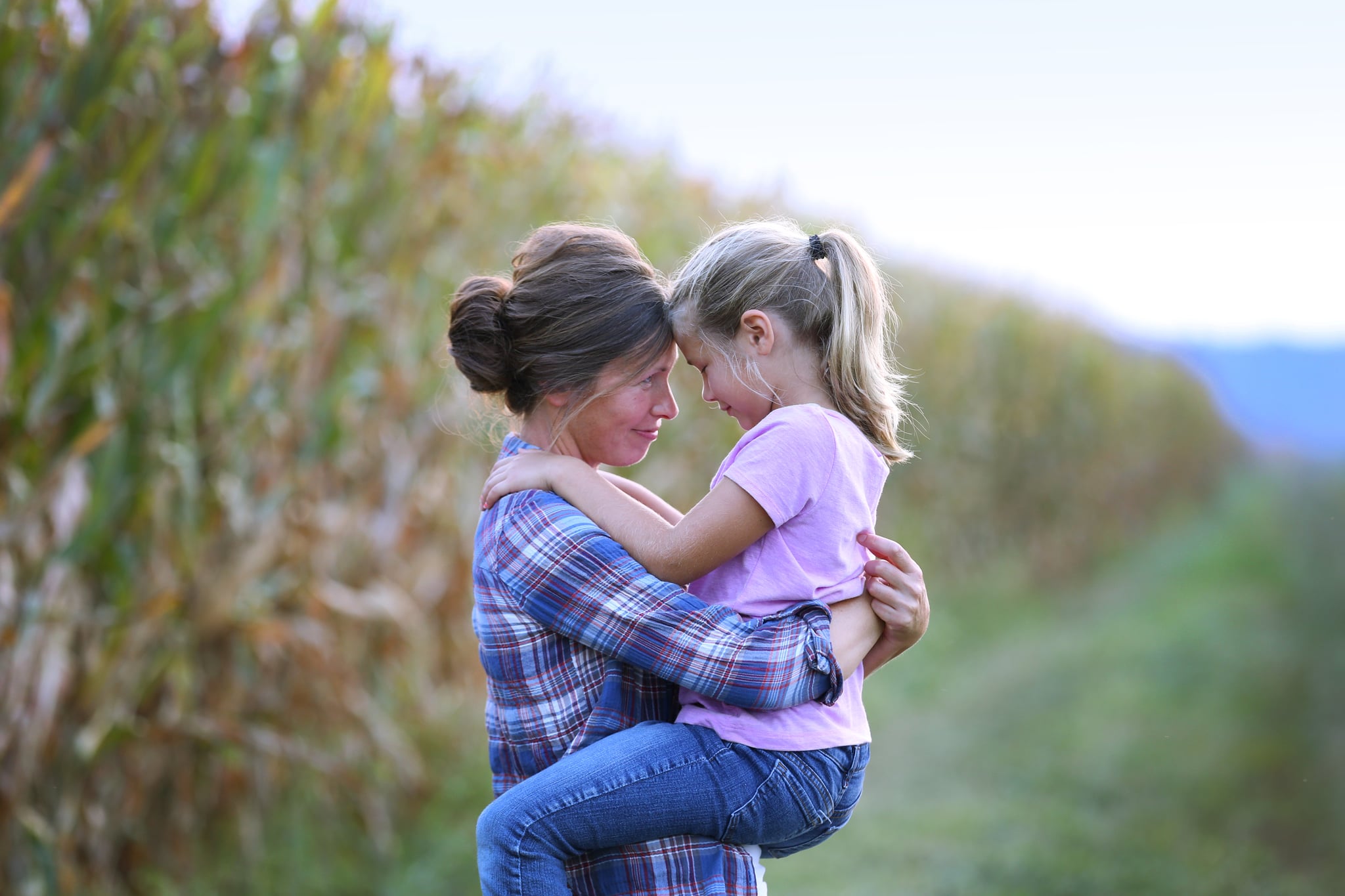 An Iowa farm mother hugs her young daughter while standing next to a field ...