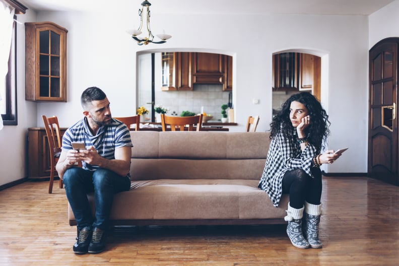 Couple in conflict sitting on sofa at home, using smart phones.