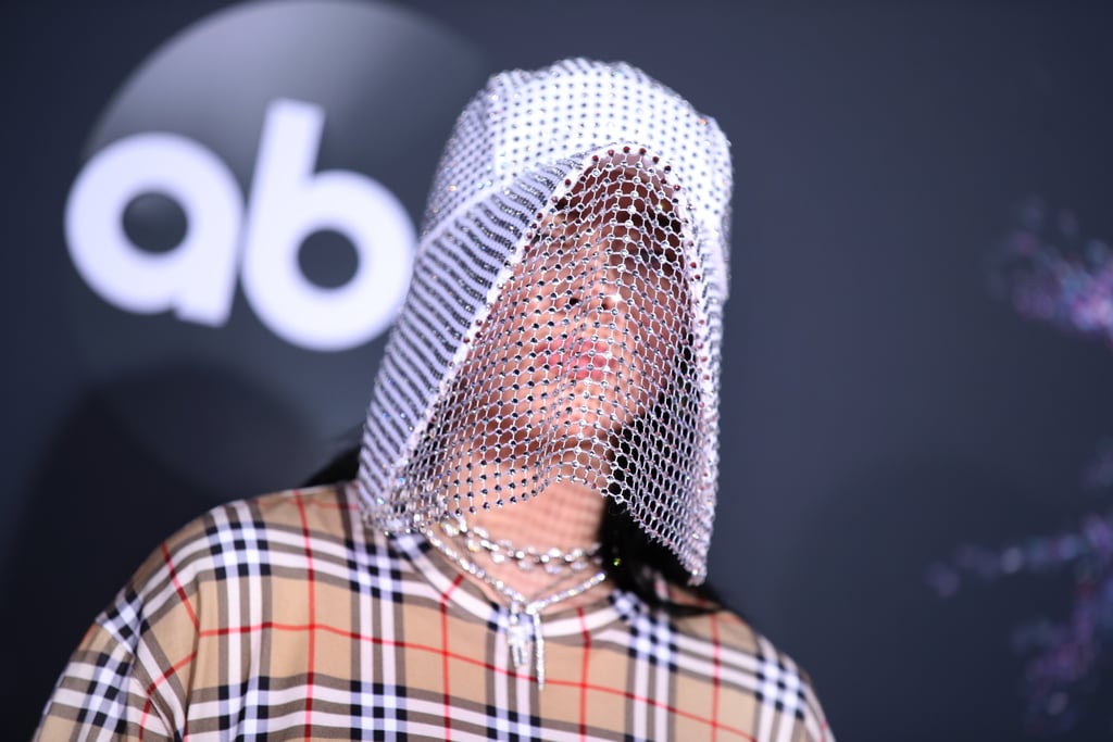 Whenever Billie Eilish hits the red carpet, you can expect to see a memorable look. And at Sunday's American Music Awards, the 17-year-old Grammy nominated singer didn't disappoint. The "Everything I Wanted" singer showed out at the Los Angeles event, rocking a plaid Burberry look with a glimmering chain mask and sneakers (because of course she can pull that off).  
Billie's first-ever American Music Awards is certainly an exciting one. Not only is she performing for the first time at an awards show, but she's also up for six honors: new artist of the year, favorite social artist, favorite pop/rock female artist, favorite alternative rock artist, favorite music video for "Bad Guy," and favorite pop/rock album for When We All Fall Asleep, Where Do We Go?. Billie's already had a successful year of topping charts and being a total boss, but we can now add her AMAs appearance to the ever-growing list of accomplishments. Look ahead to see all the pictures from her night at the ceremony!