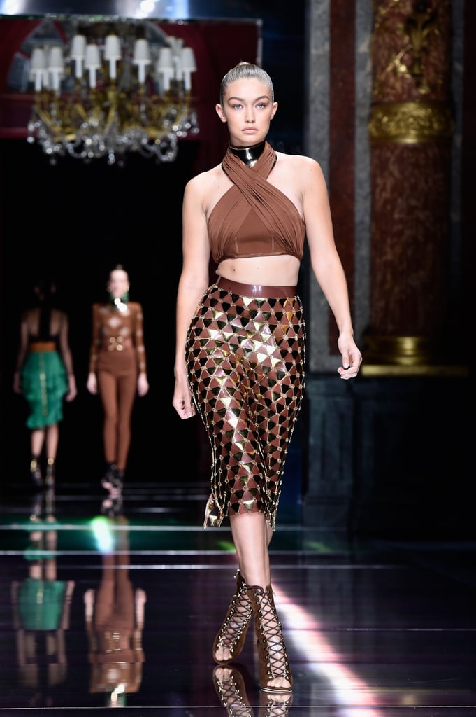 Gigi's Spring '16 Balmain ensemble consisted of a twisted halterneck crop top, gold statement choker, and flashy gold-plated midi skirt. Her look was complete with luxe, strappy brown lace-ups.