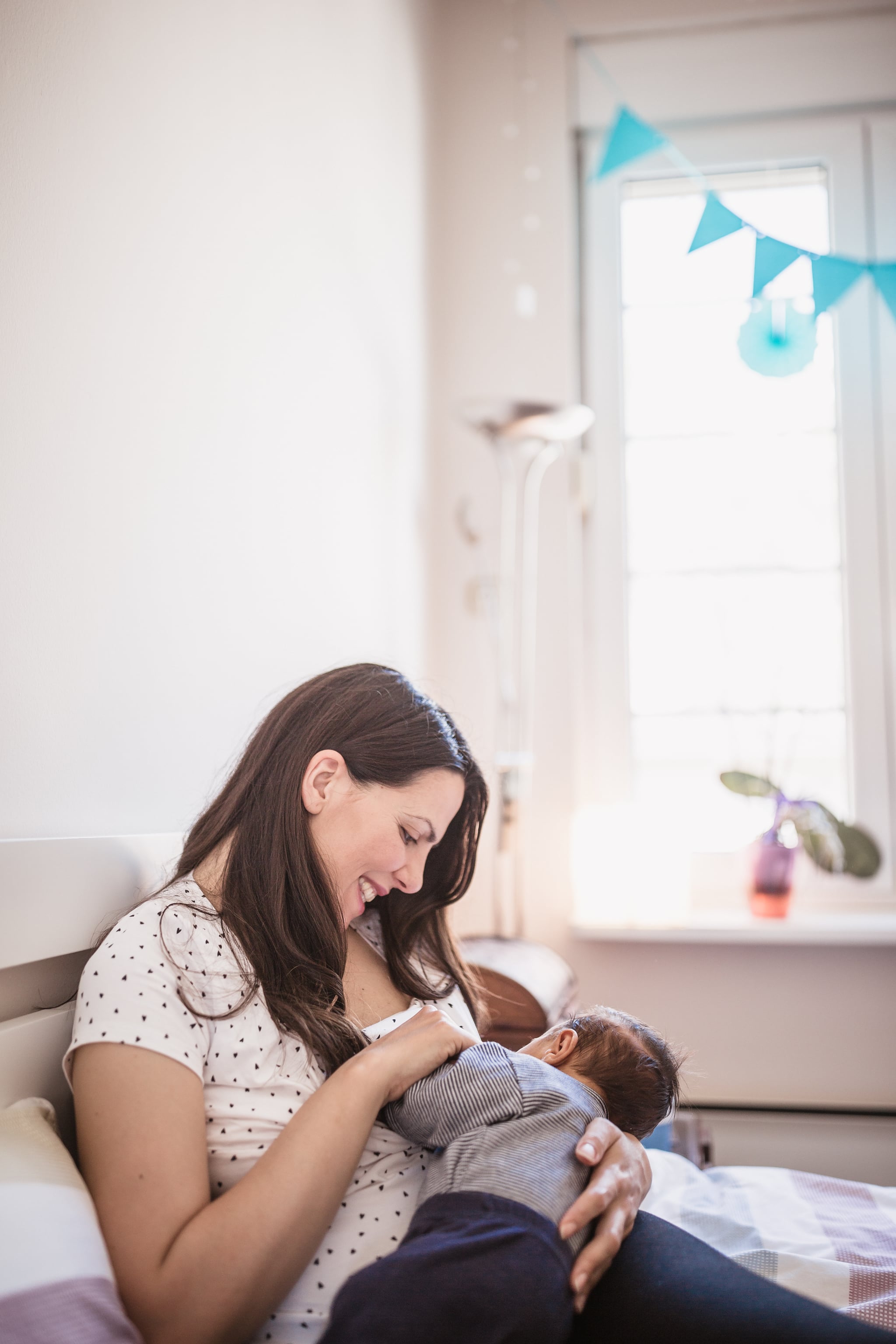 Mother and newborn baby boy are indoors in bedroom. Mother is breastfeeding her son while lying in bed.