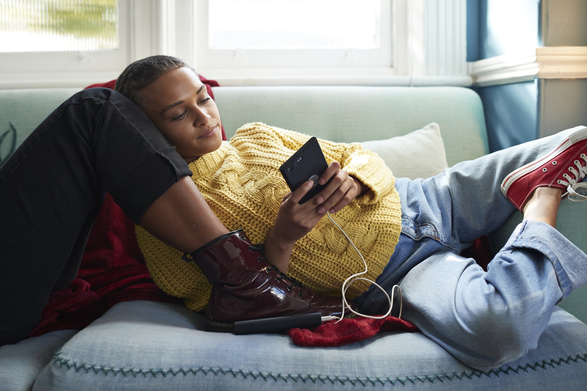 Woman using mobile phone while leaning on friend's leg at home