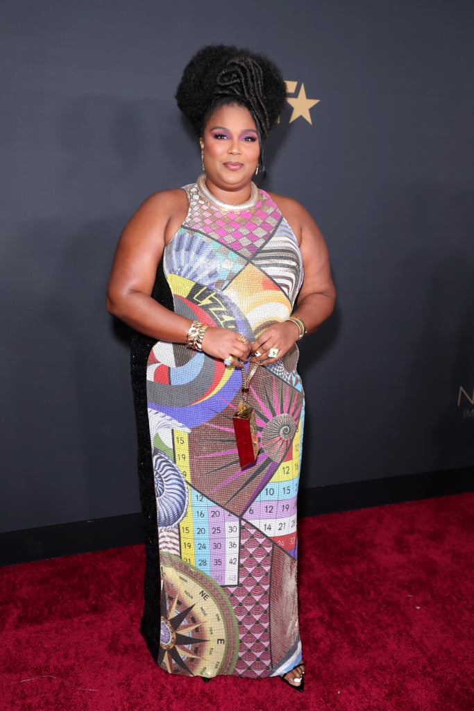 Lizzo looked "good as hell" at the NAACP Image Awards on Saturday night, but what else is new? The "Truth Hurts" singer accepted the prize for entertainer of the year during the show, and looked incredible decked out in a custom Mary Katrantzou gown. The dress was designed with geometric shapes covering chainmail and featured Lizzo's name printed across the front — a permanent reminder that this outfit is one of a kind! 
Lizzo's stylist, Brett Alan Nelson, tied the look together with pointed sandals from Smash Shoes and a 24K gold bar clutch from Lynn Ban. The bag? Lizzo has it secured. Keep reading for more glimpses of Lizzo's look from all angles.