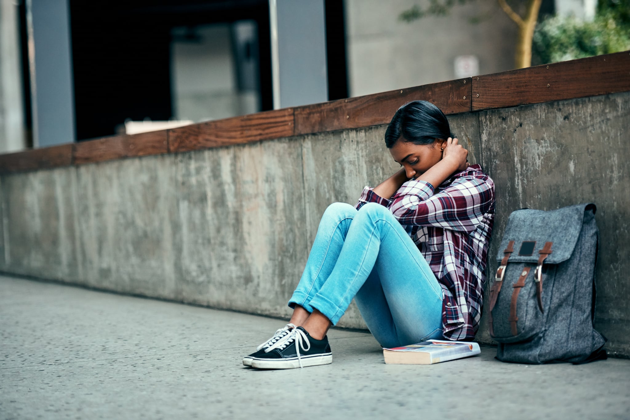 Shot of a young female student sitting on the floor feeling depressed outside on campus