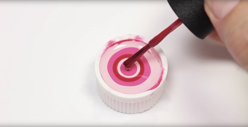Fill a small bottle cap with room temperature water. Pro tip: filtered water works best.
Drop a bit of each color into the filled bottle cap.
Use a toothpick and carefully drag it through the middle of the cap to form a heart.
Let the polish masterpiece dry inside the caps for about 1-2 hours.