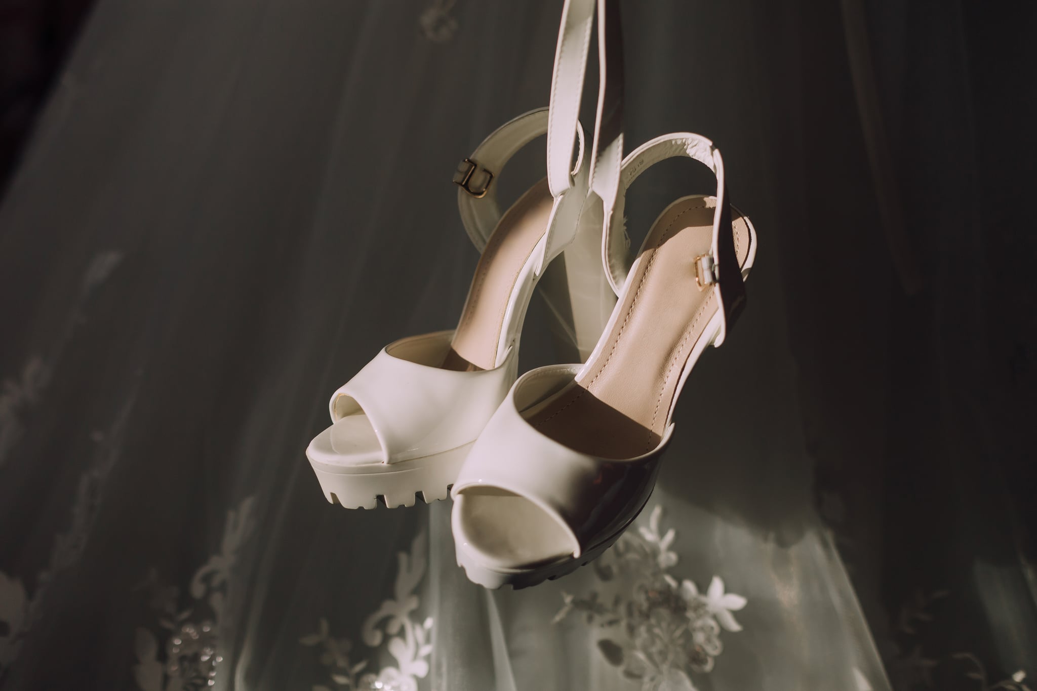 Two white high heels are hanging from a curtain. The shoes are on display, possibly for a wedding or other special occasion. The image has a romantic and elegant mood
