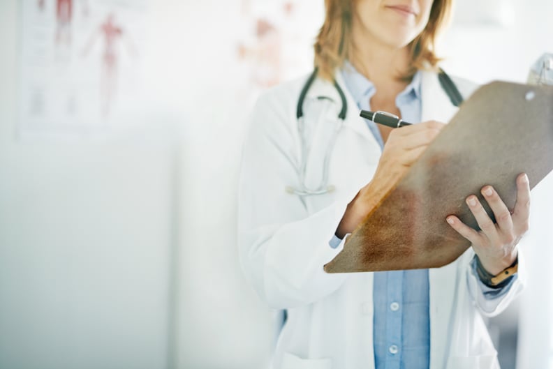 Cropped shot of a doctor writing on a clipboard in a consulting room