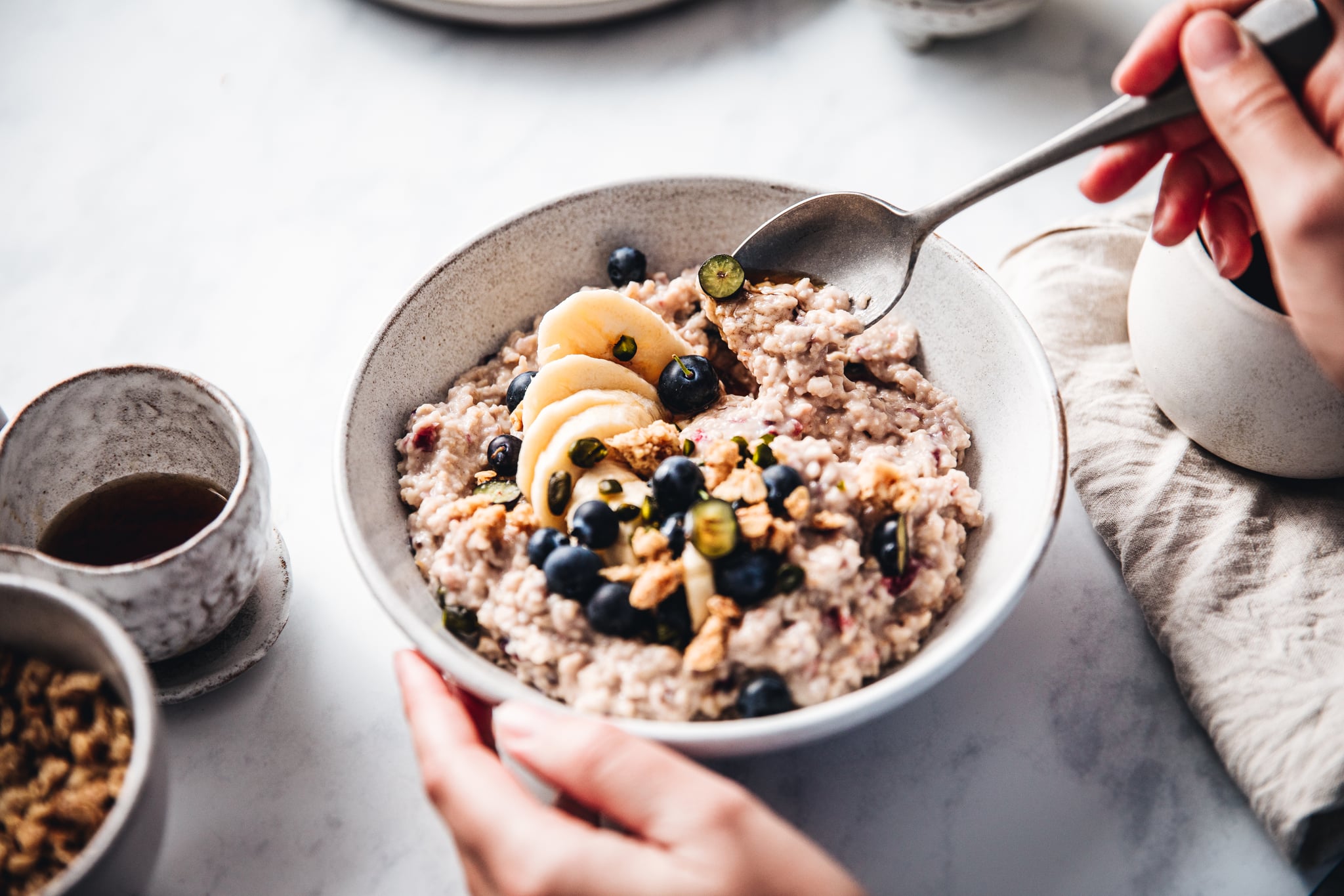 Close-up of a woman mixing oats flour, banana and blueberries in a bowl. Female making healthy breakfast in kitchen.