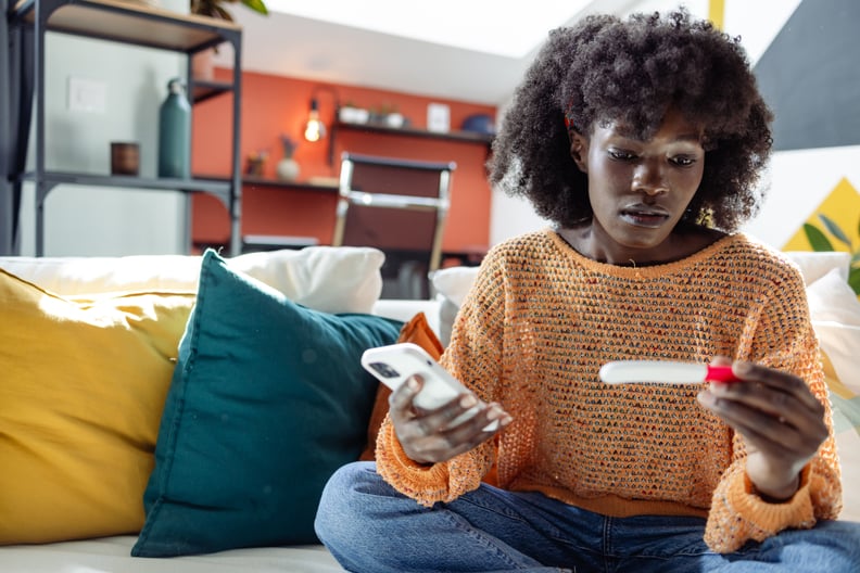 A young African American woman is looking at the home pregnancy test while holding a smart phone, googling what is ectopic pregnancy 