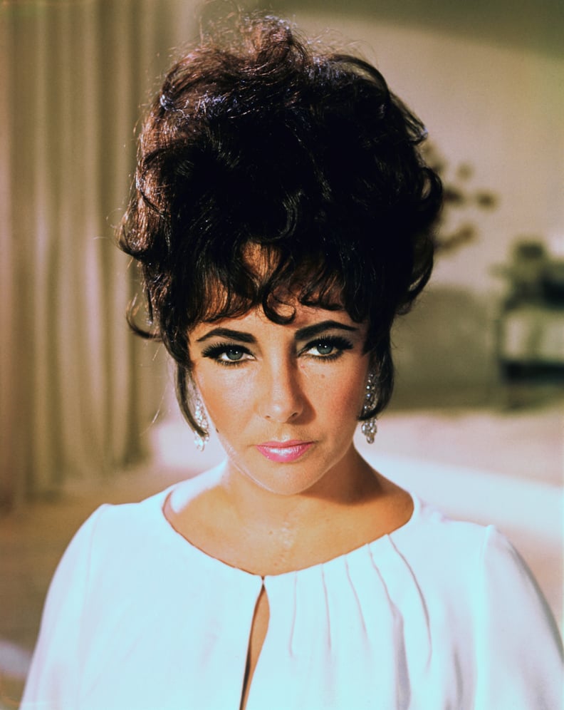 Publicity handout of actress Elizabeth Taylor, shown from the shoulders up, wearing a white dress, with her hair pinned up loosely to form a bouffant. Undated photograph.