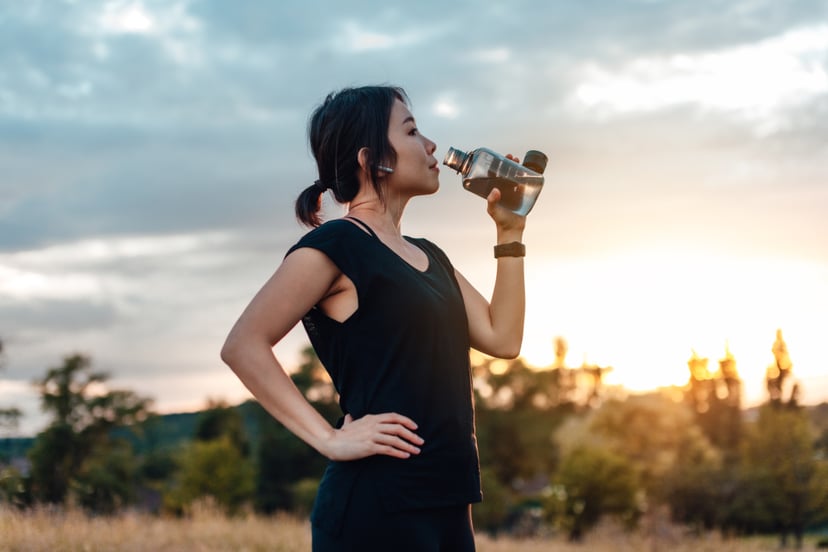 Young woman taking a break from running, against sunset. Beautiful young sport woman is drinking water, exhausted after the daily training