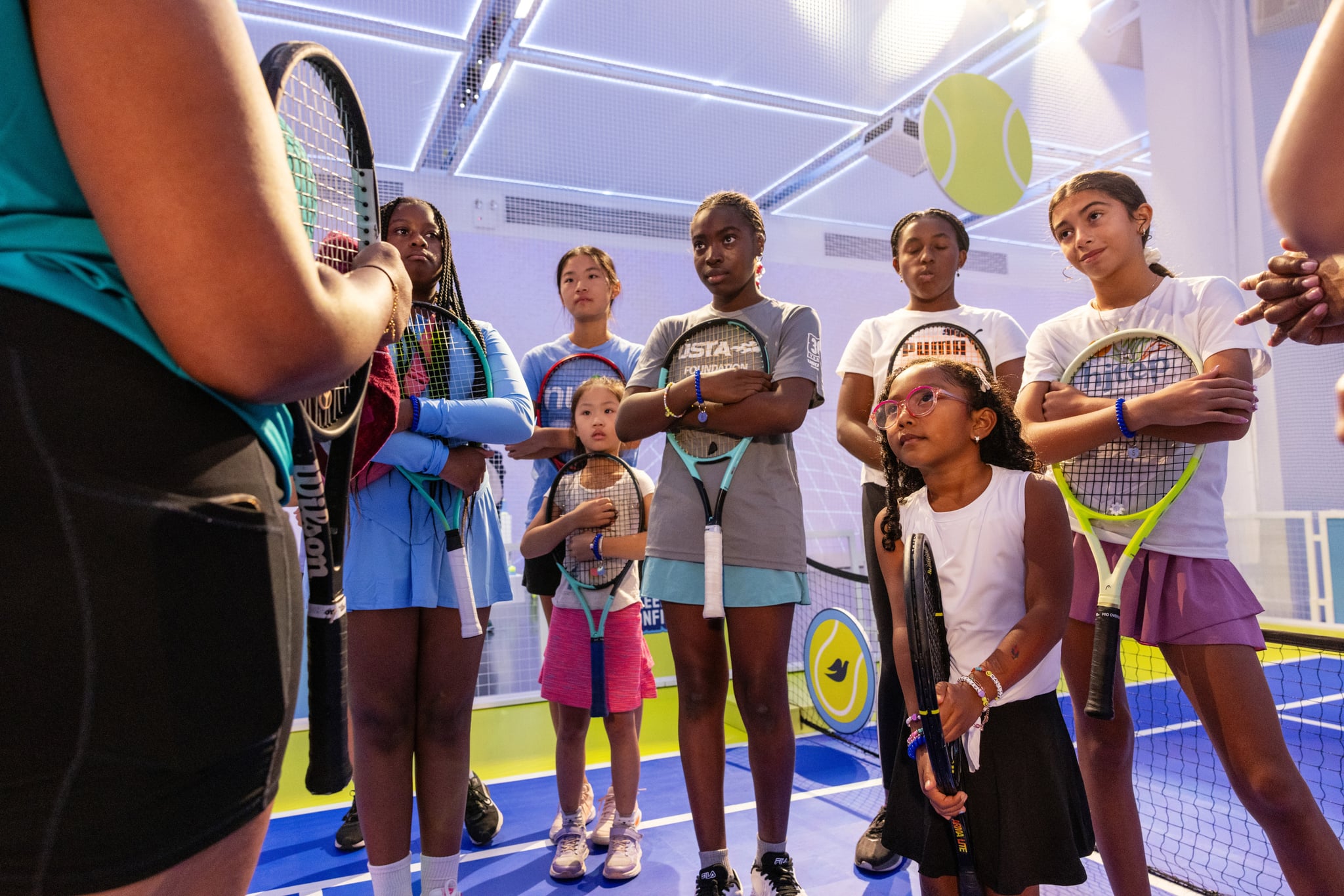 Young girls of various ethnicities holding their tennis rackets on a blue and green tennis court at Dove's Body Sport Program event with Venus Williams and Black Girl Tennis Club.