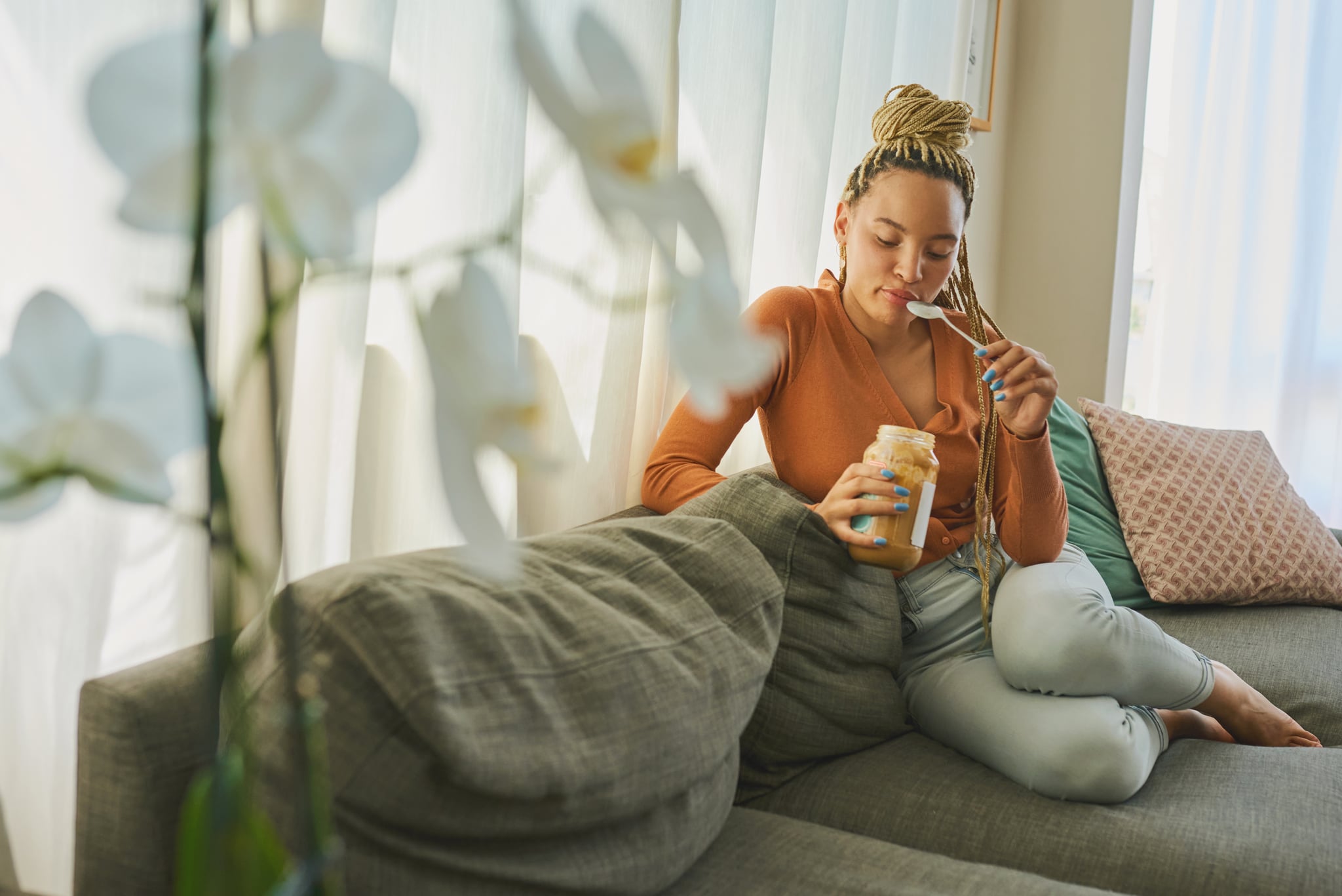 woman sitting on couch eating peanut butter wondering if peanut butter is healthy and good for you