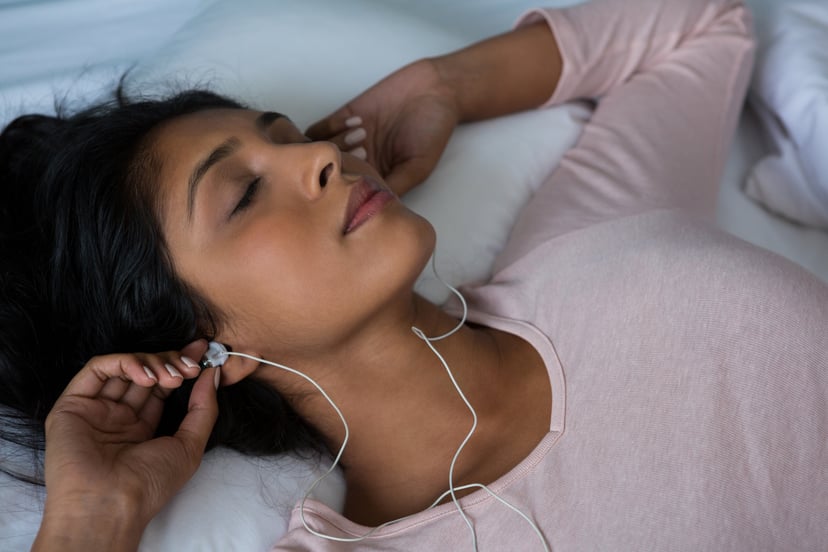 Young woman sleeping while listening to music on bed