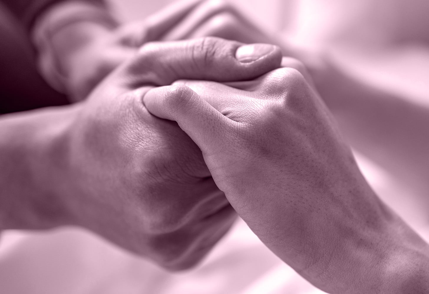 Two people holding hands on pink background.