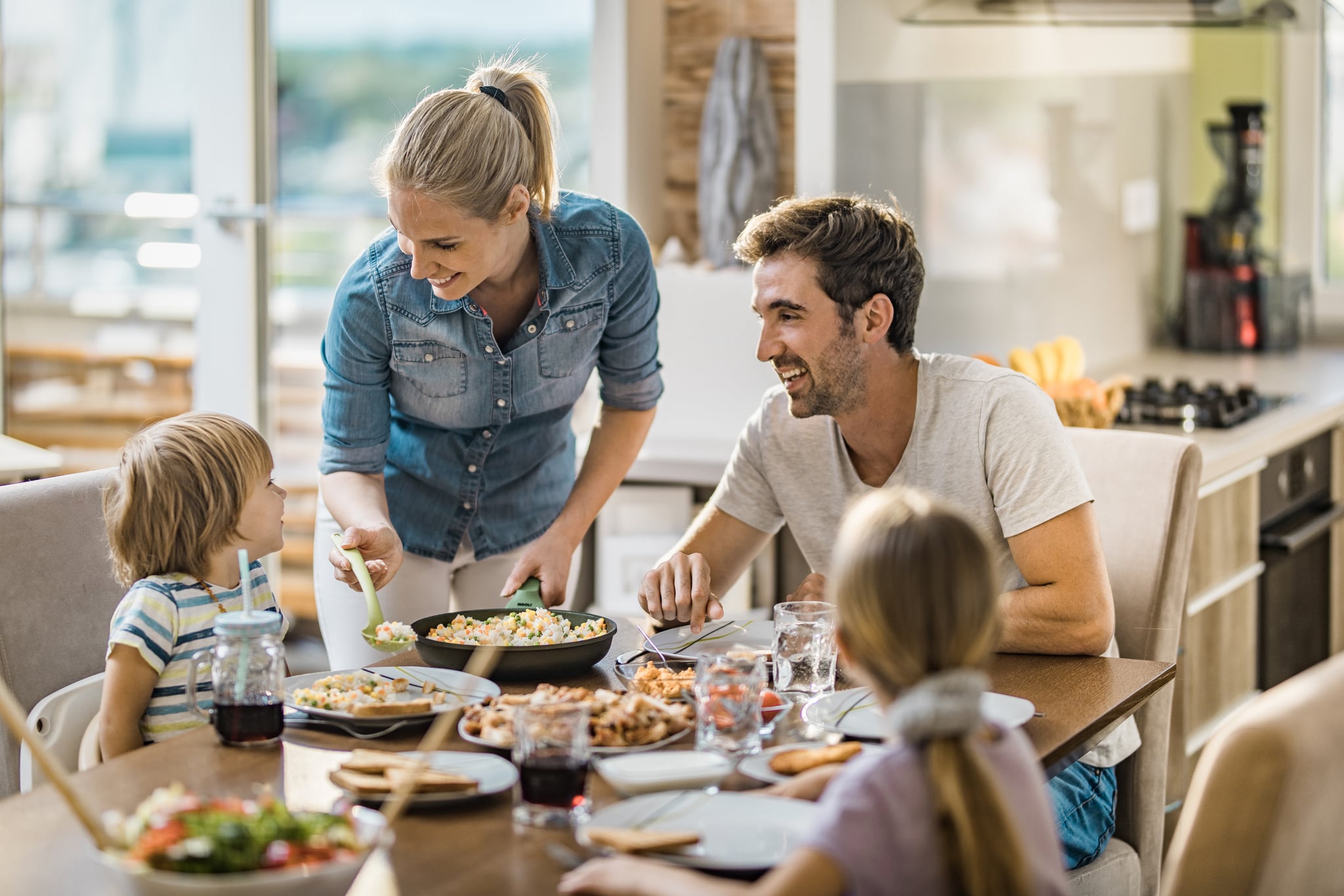 Happy woman serving food to her family in dining room while talking to her small son.