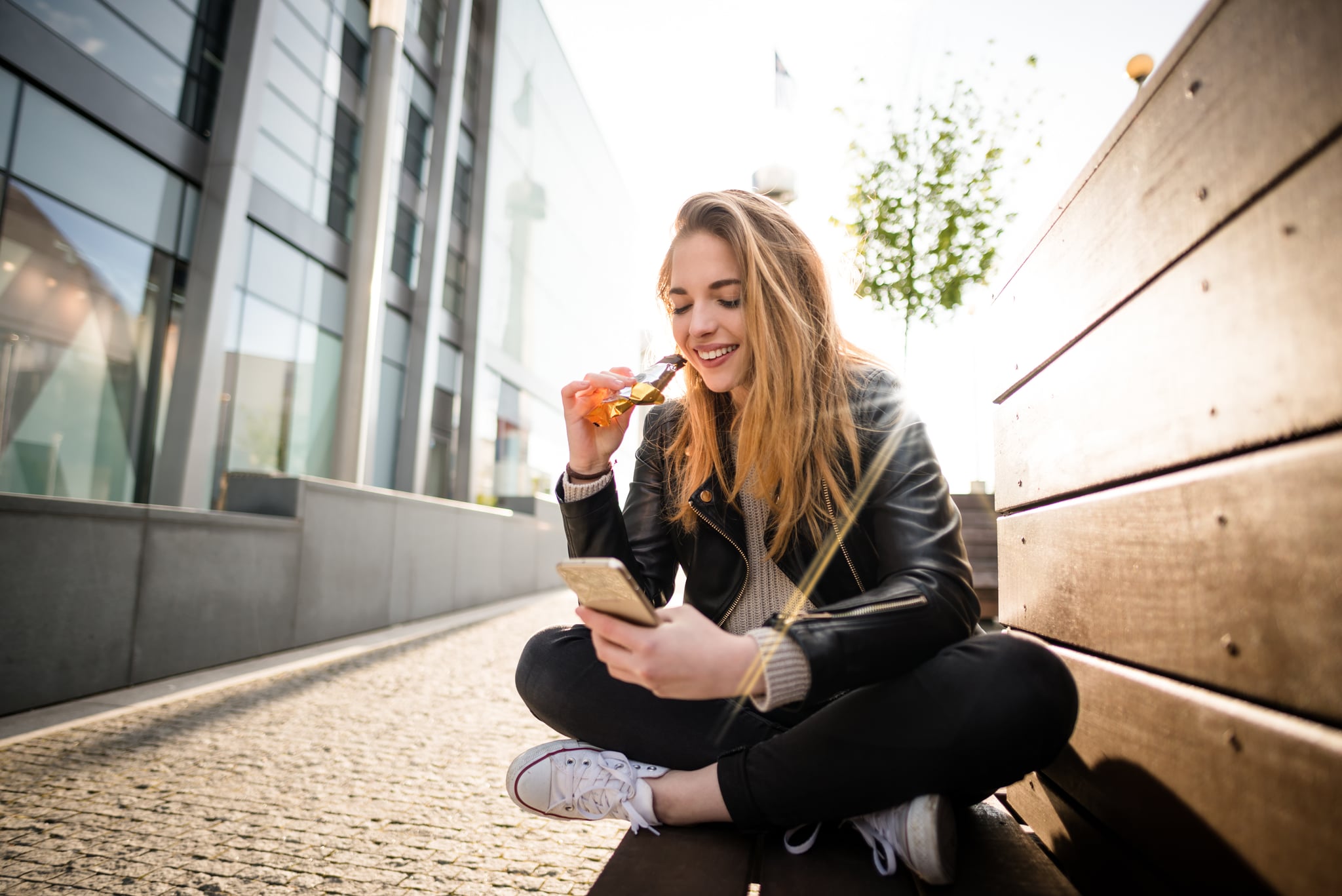 Wide angle photograph of teenager eating chocolate on phone outddoor in street - against sun with lens flare