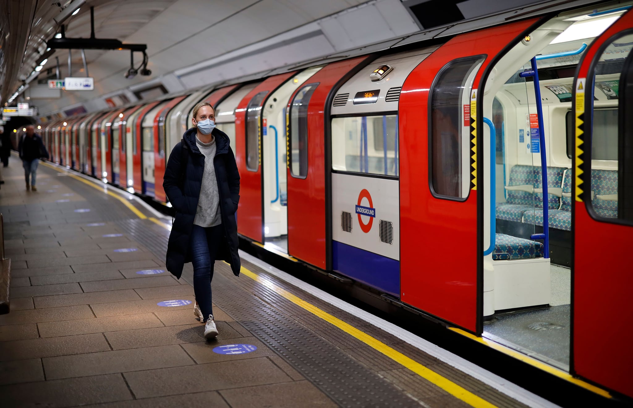 A woman wearing PPE (personal protective equipment), including a face mask as a precautionary measure against COVID-19, walks along the platform alongside a London Underground Tube train in the morning rush hour, on May 11, 2020, as life in Britain continues during the nationwide lockdown due to the novel coronavirus pandemic. - British Prime Minister Boris Johnson on May 10 announced a phased plan to ease a nationwide coronavirus lockdown, with schools and shops to begin opening from June 1 -- as long as infection rates stay low. (Photo by Tolga Akmen / AFP) (Photo by TOLGA AKMEN/AFP via Getty Images)