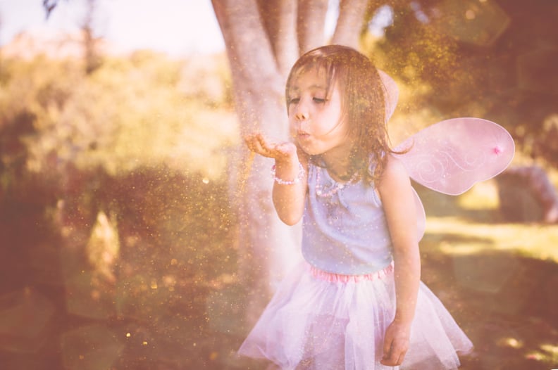 Asian girl dressed as fairy blowing glitter and having fun in the garden in spring