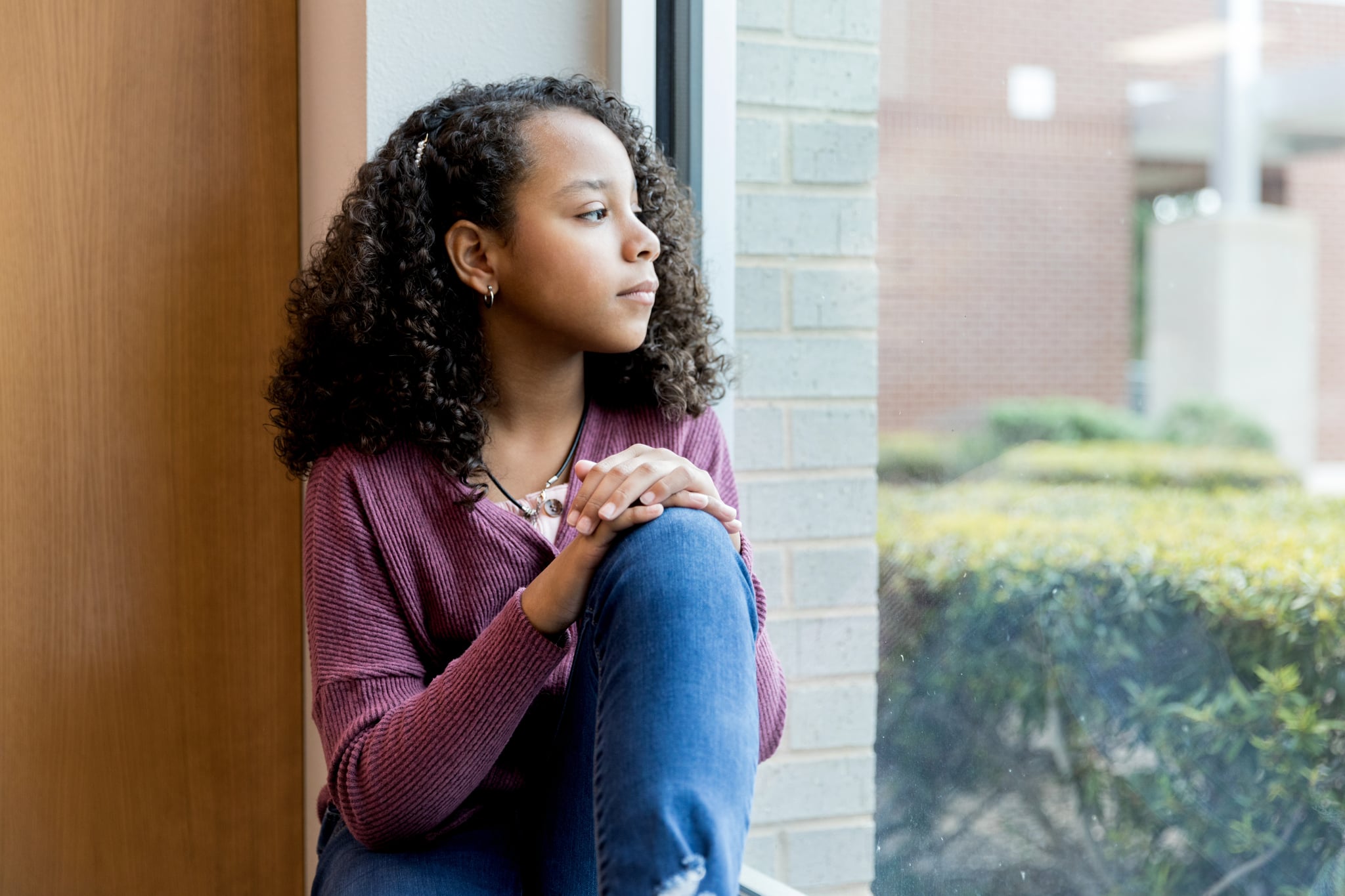 Lonely mixed race preteen schoolgirl day dreams as she looks through the window while at school.