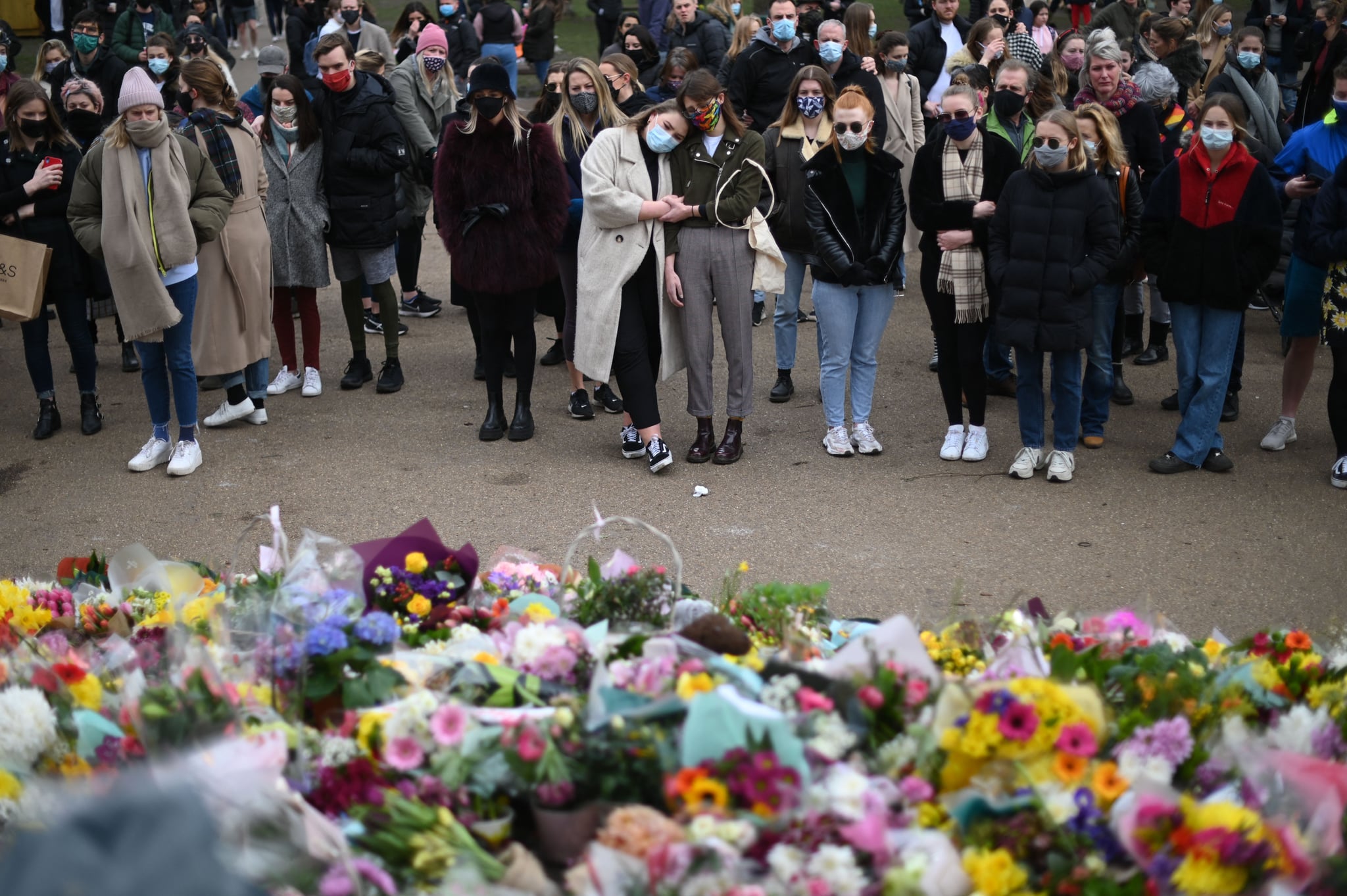 Well-wishers react as they gather at floral tributes to honour Sarah Everard, the missing woman who's remains were found in woodland in Kent, at the bandstand on Clapham Common in south London on March 14, 2021. - London's Metropolitan Police on March 14 defended its handling of a high-profile protest calling for greater public safety for women, after male officers were seen scuffling with the crowd and physically restraining female demonstrators. Hundreds defied coronavirus restrictions on March 13 night to gather on Clapham Common park to mark the death of Sarah Everard, who went missing nearby as she walked home earlier this month. A serving police officer with the London force has since been charged with her kidnap and murder. (Photo by DANIEL LEAL-OLIVAS / AFP) (Photo by DANIEL LEAL-OLIVAS/AFP via Getty Images)