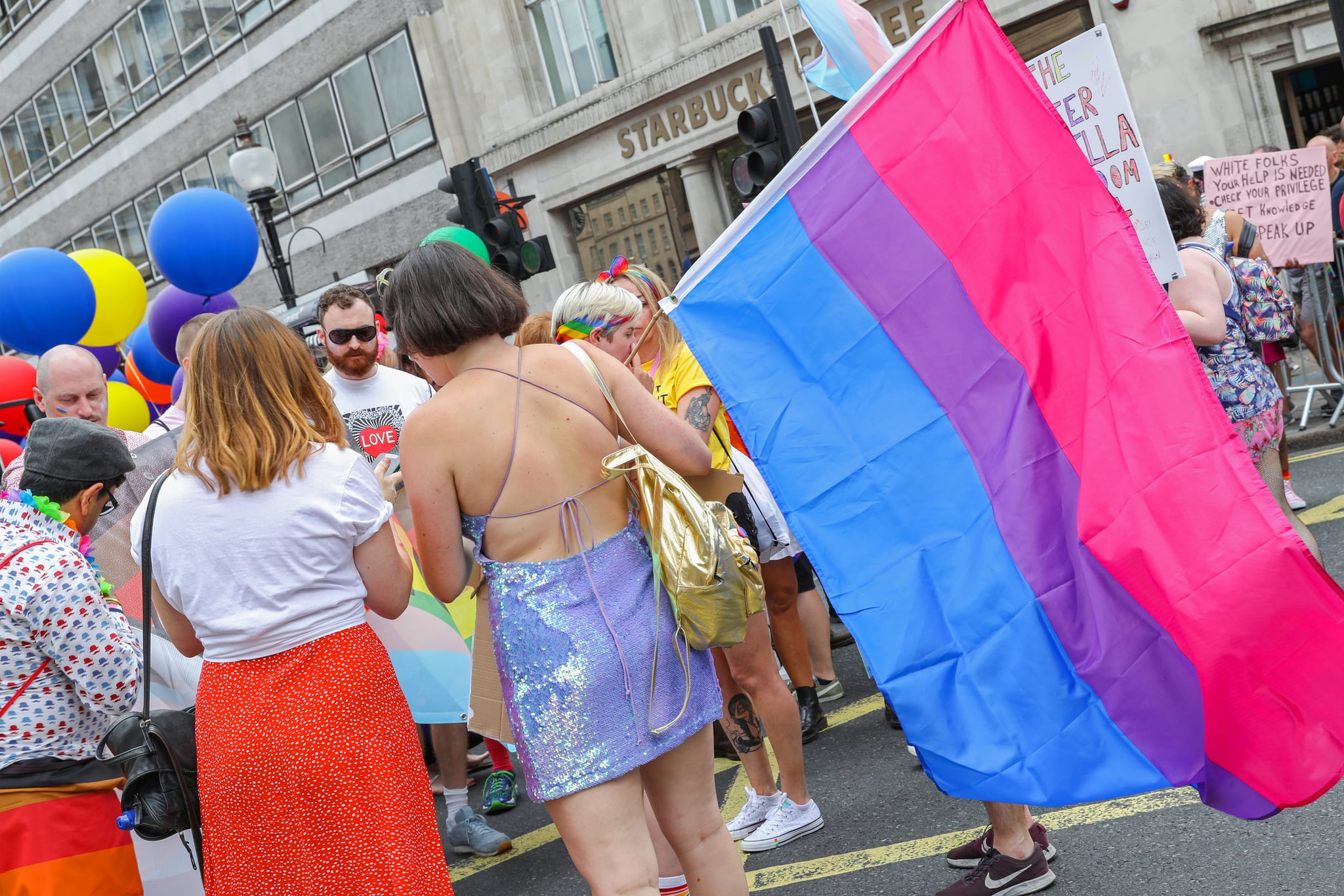 Parade goers in London stand at a Pride celebration, with one holding the the bisexual pride flag, which has pink, purple, and blue colors. (Photo by Tristan Fewings/Getty Images for Pride in London)