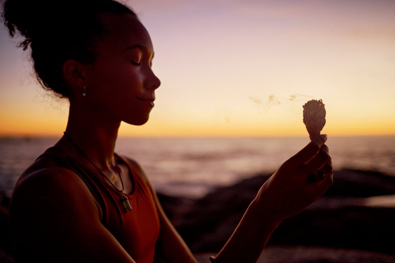 Sunset meditation, woman relax in by beach and ocean for zen peace focus, chakra wellness and mental health by the sea. Burning sage in nature, aromatherapy and spiritual mindfulness health exercise