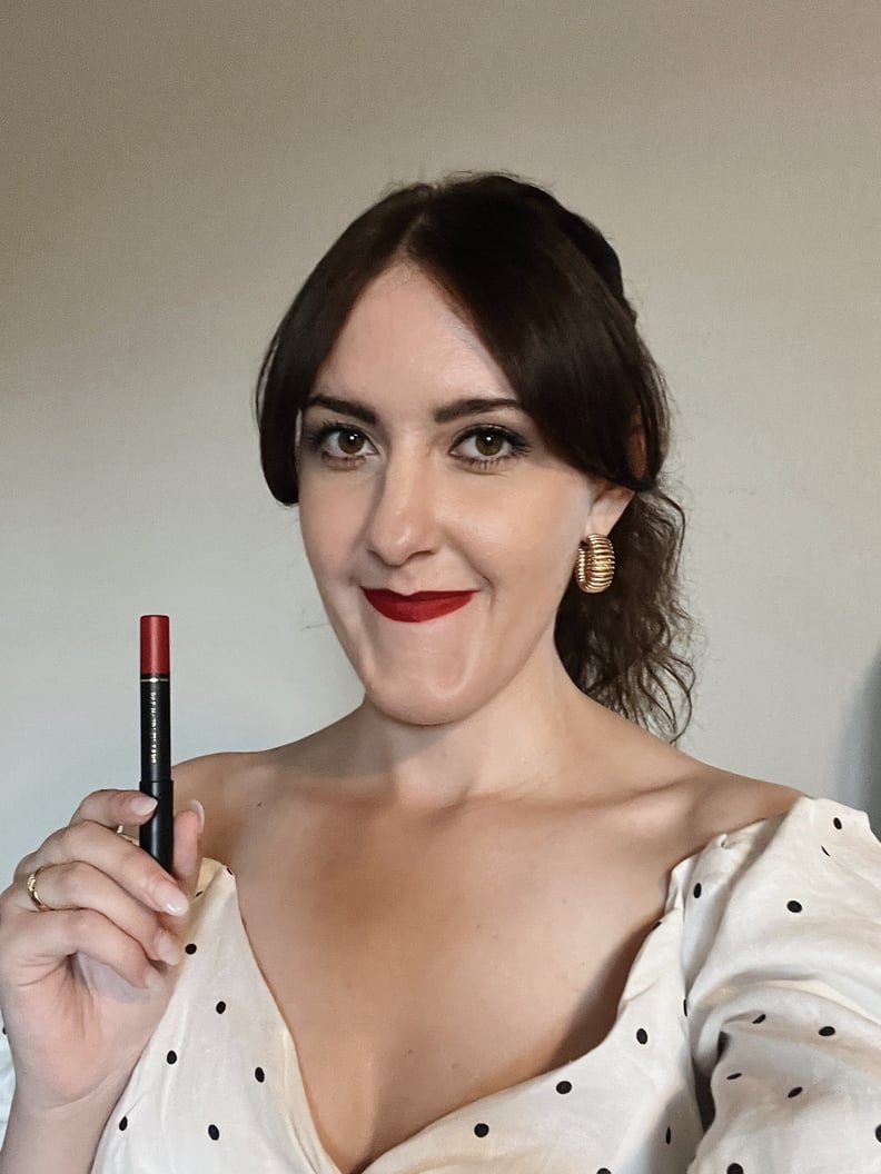 Mujer sonriendo mientras sostiene el lápiz labial Dramatique Mega Lip Pencil de Pat McGrath Labs en color rojo Elson