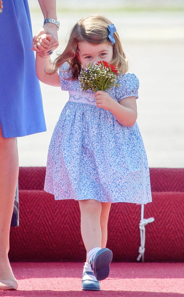 Princess Charlotte looks sweet wearing a blue floral smocked dress as she smells her bouquet.