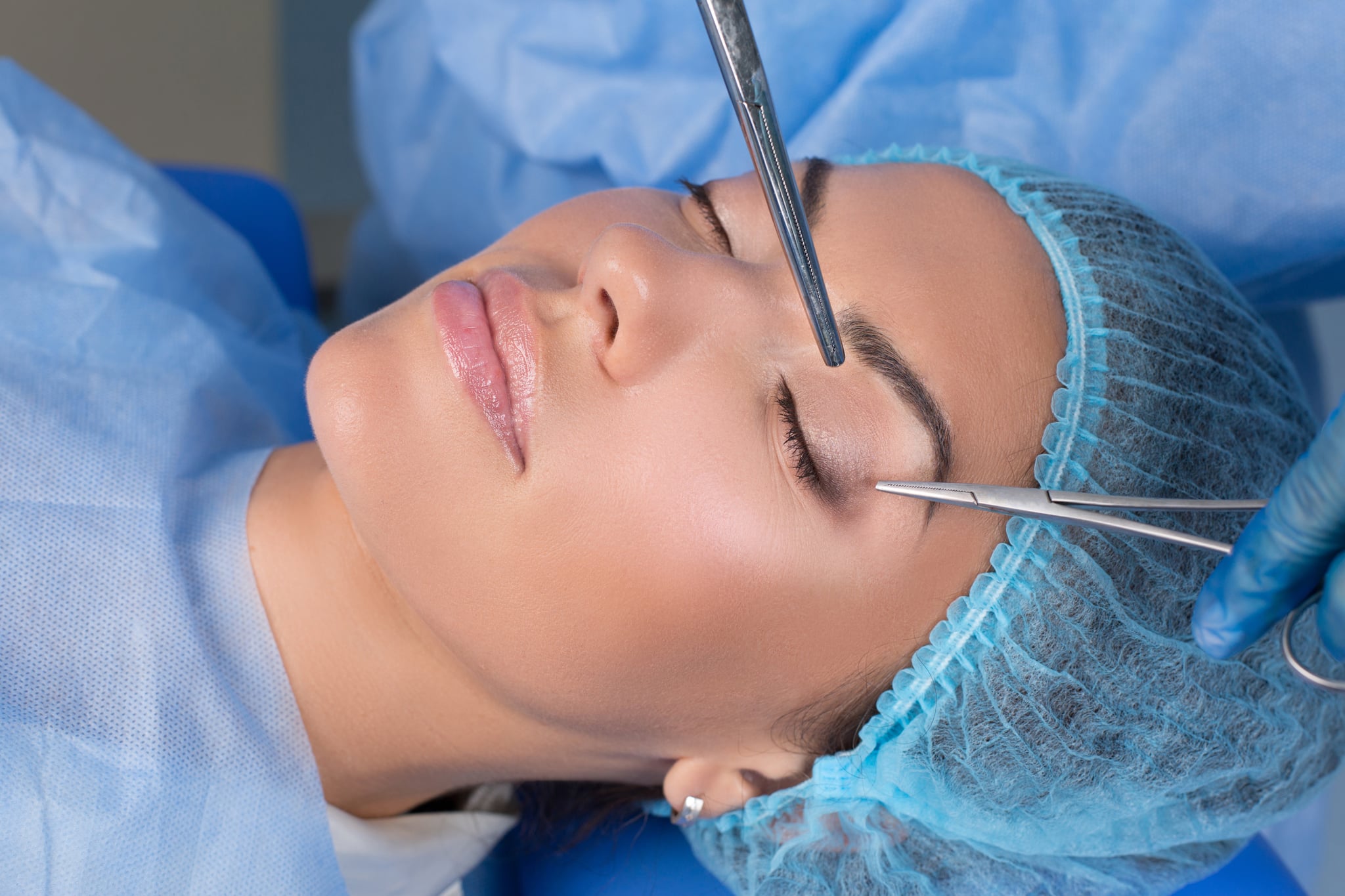 Upper eyelid blepharoplasty. Beautiful middle age woman getting ready for eyelid lift plastic surgery doctor hands in blue gloves point medical tools to her eye. Beauty, people and health concept